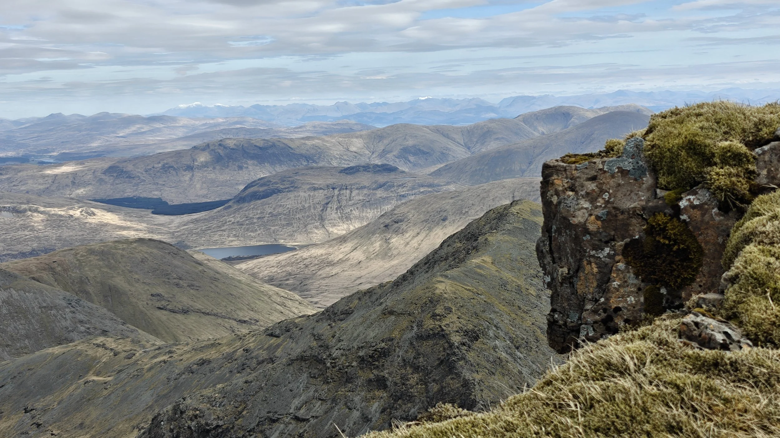 Paysage montagneux avec sommets, vallées, un lac, et des rochers recouverts de mousse et de végétation