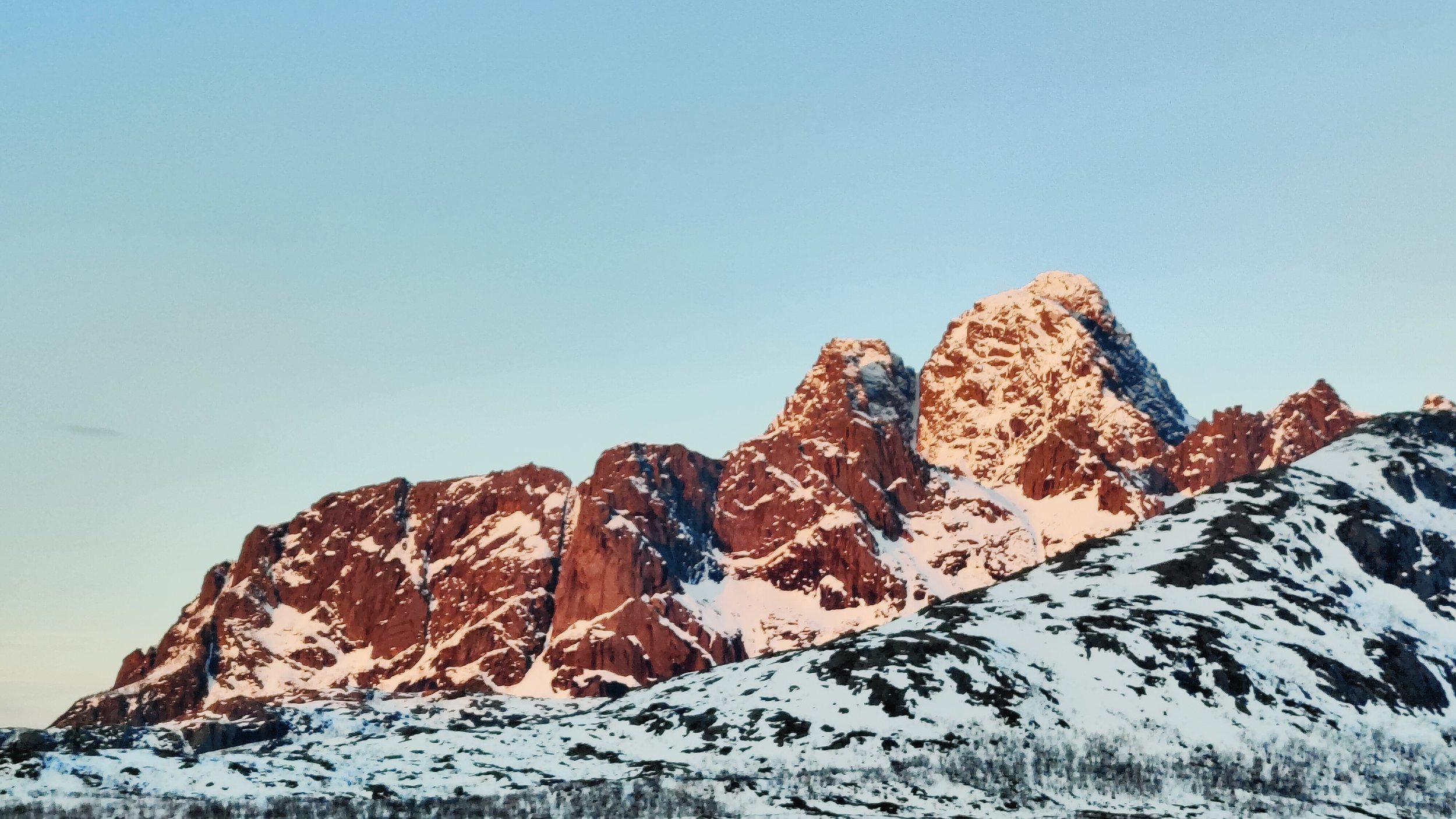 Montagnes rocheuses enneigées au coucher du soleil, avec un ciel clair.