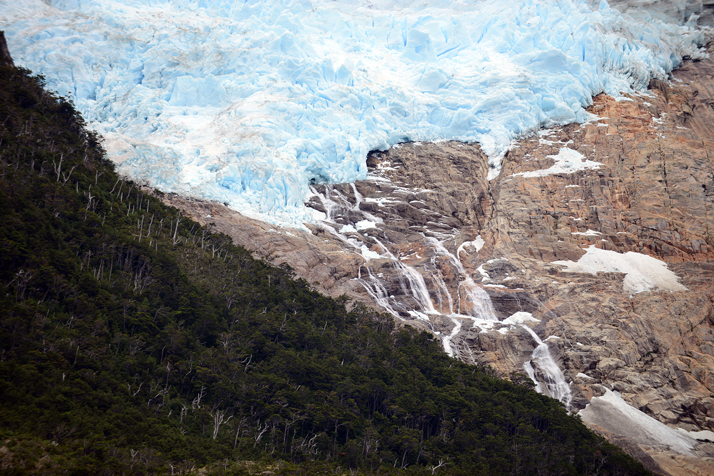 Cascade de glace coulant sur une paroi rocheuse, avec une forêt verte en contrebas.