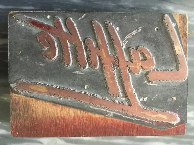 Une plaque en métal avec le mot gravé 'JACK' en lettre majuscule, fixée sur une surface en bois.