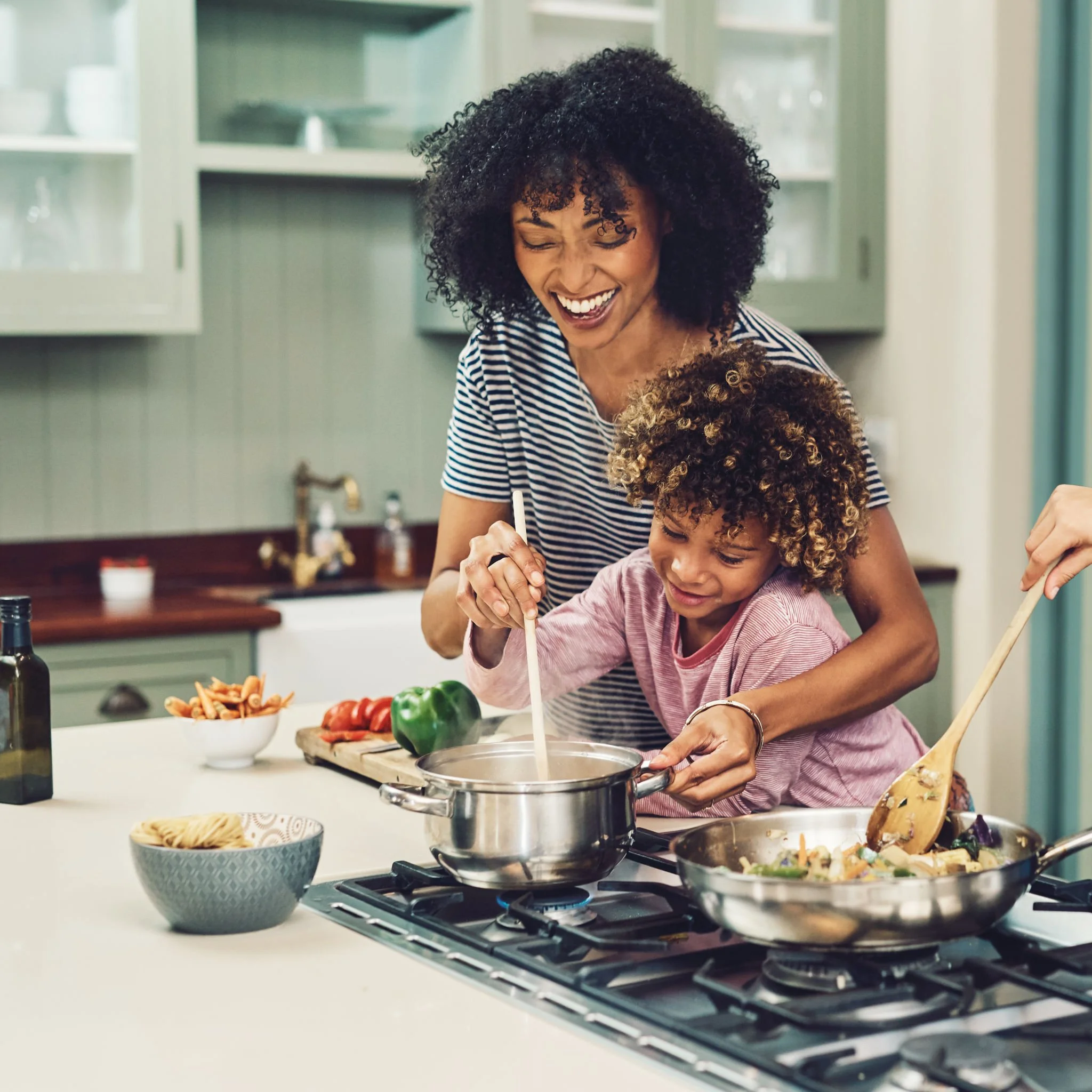 A woman and a young girl cooking together in a kitchen, stirring a pot on the stove and smiling.
