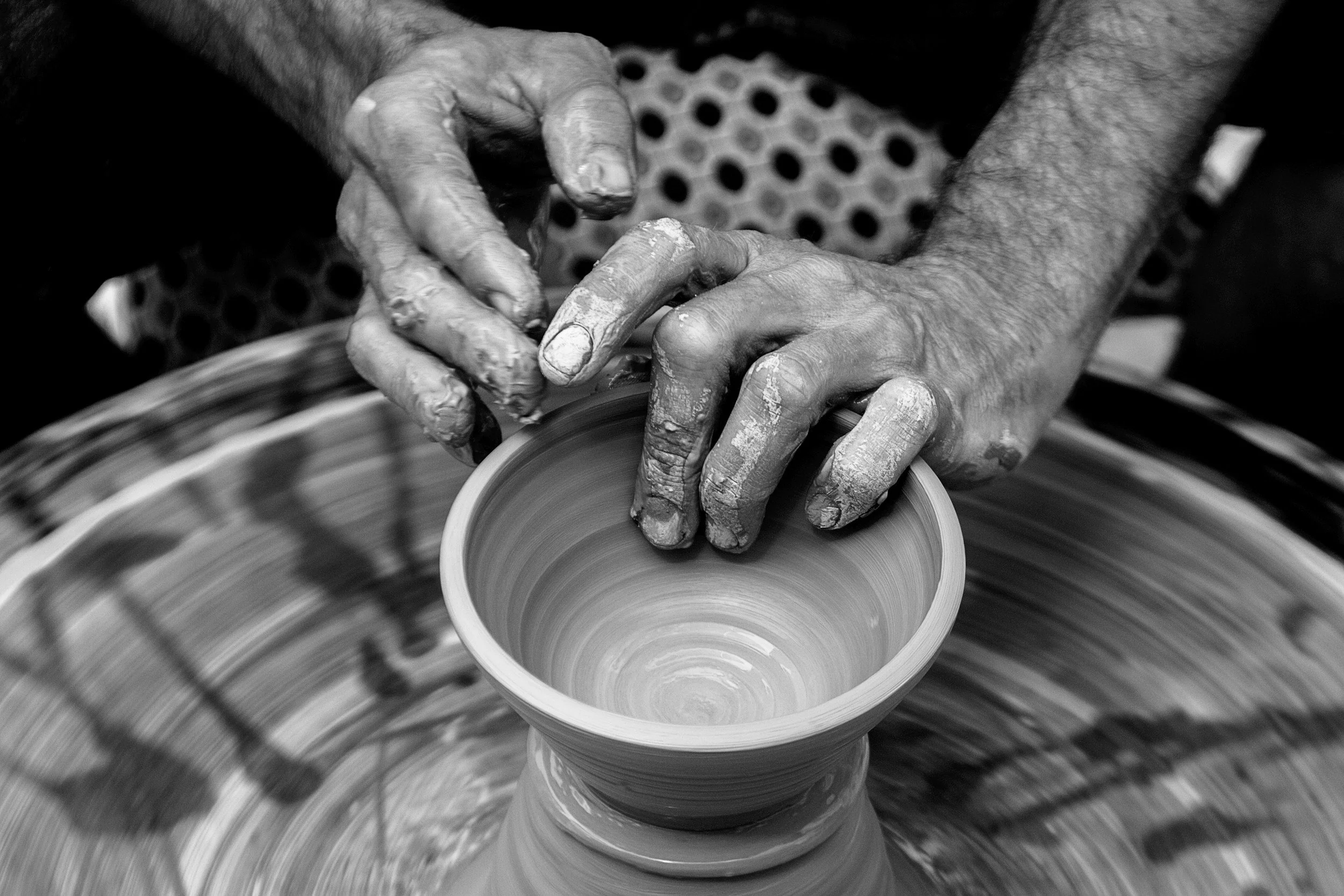 A person shaping a clay vase on a pottery wheel with their hands covered in wet clay.