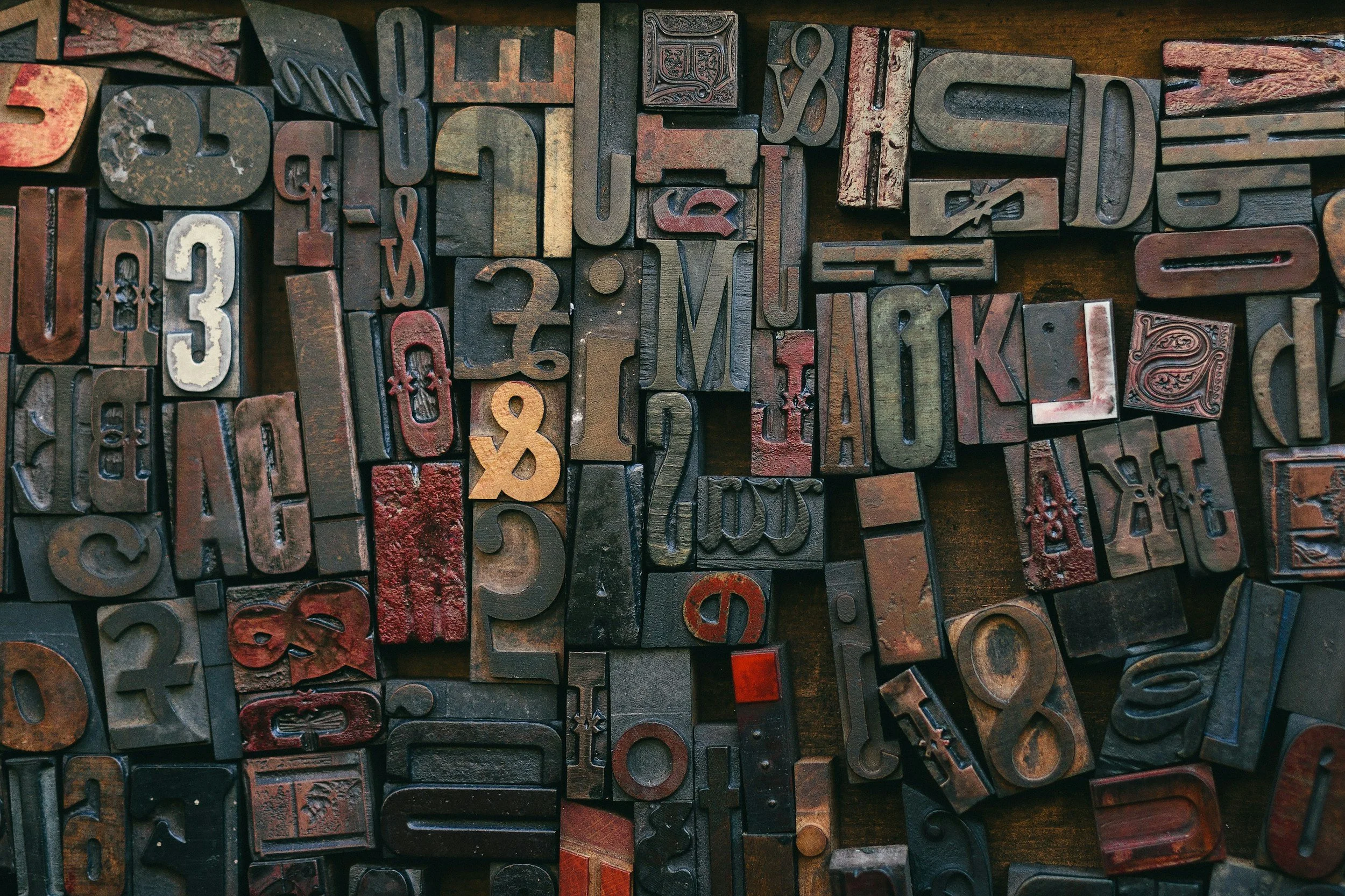 A collection of old, vintage letterpress printing blocks with raised letters and numbers arranged haphazardly on a wooden surface.