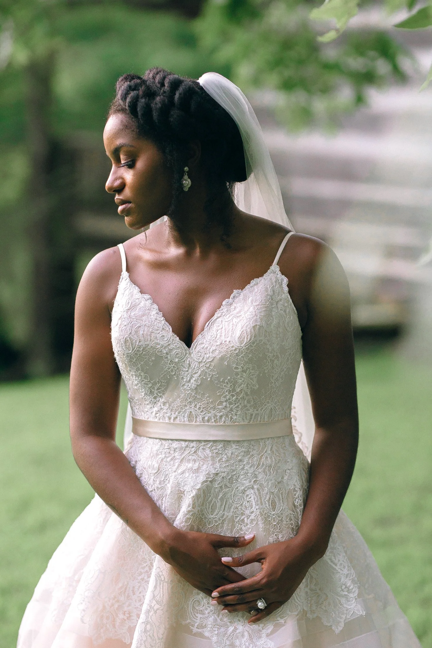 A bride in a white wedding dress with lace details and a veil, standing outdoors with greenery in the background for a Memphis Based wedding. Wedding Photography by Sowing Clover Photography.