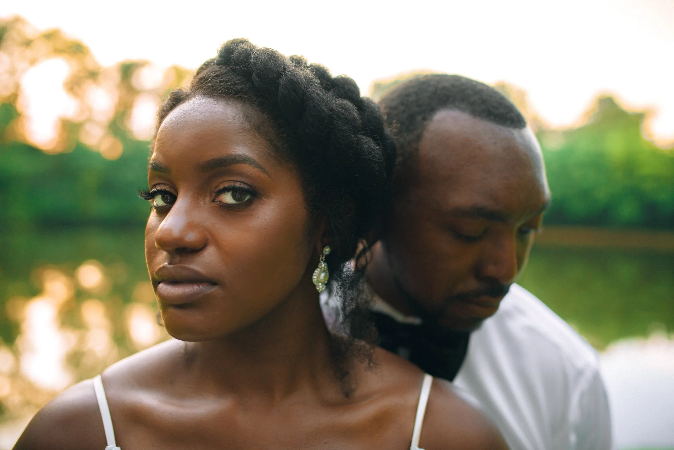 A bride with braided hair wearing jewelry and a white wed dress, looking directly at the camera, standing next to a groom for a Memphis based wedding. Wedding Photography by Sowing Clover Photography.