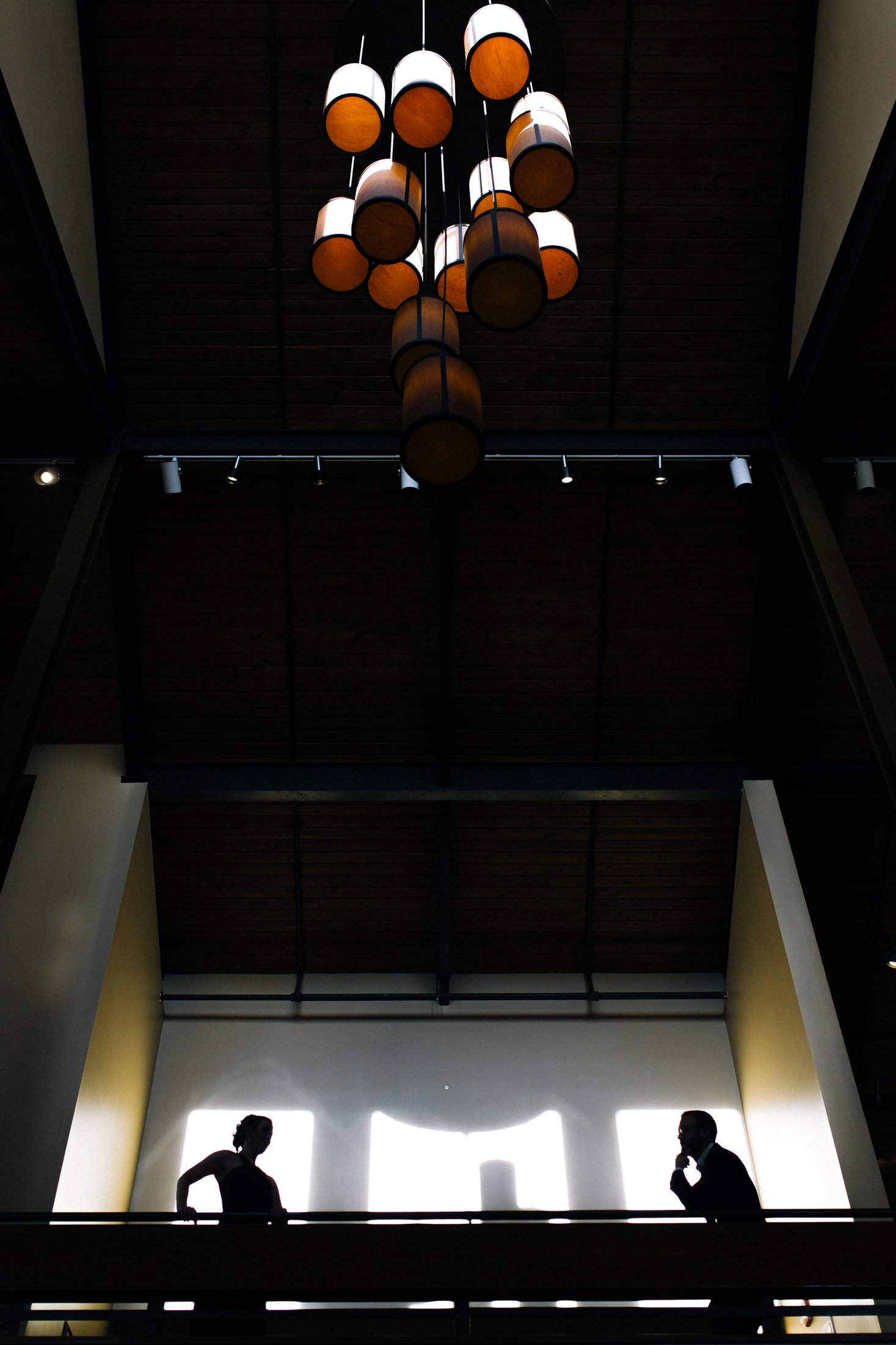Silhouettes of a man and woman standing and talking in a modern building interior with a chandelier hanging from the ceiling in North Georgia. Wedding Photography by Sowing Clover Photography.