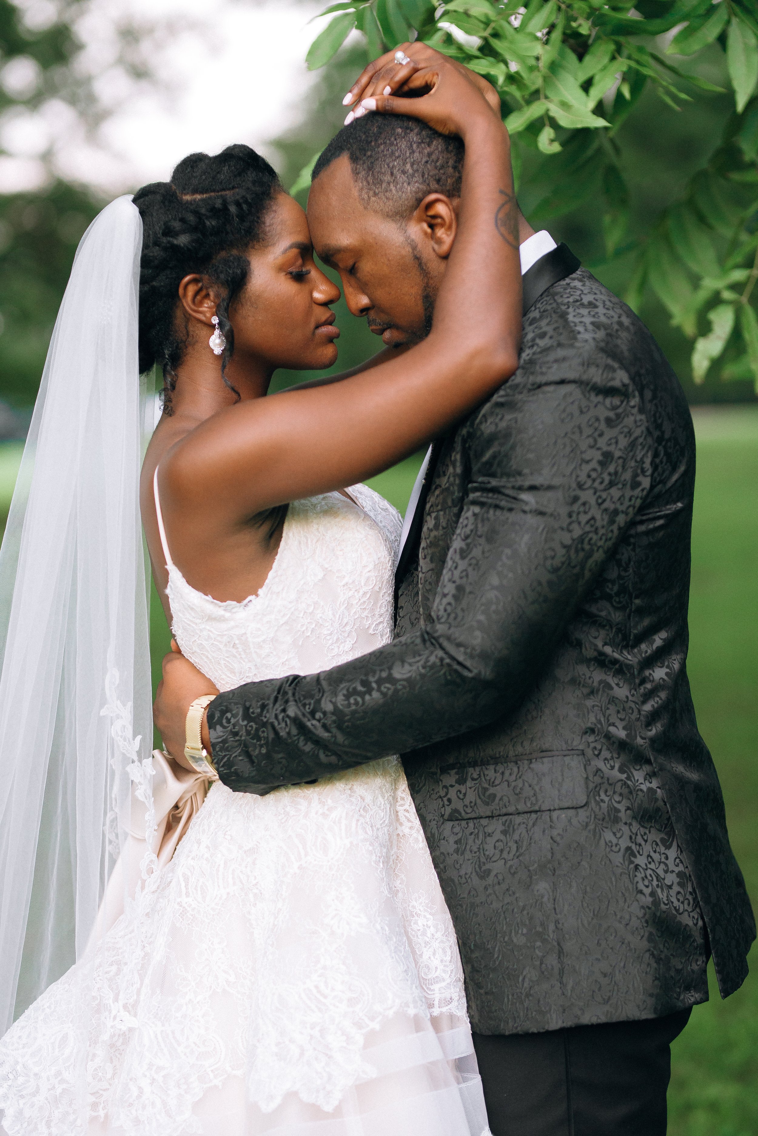 A bride and groom share a close, intimate moment outdoors, with their foreheads touching and eyes closed, surrounded by lush greenery. Memphis Tn, Wedding photography by Sowing Clover Photography.