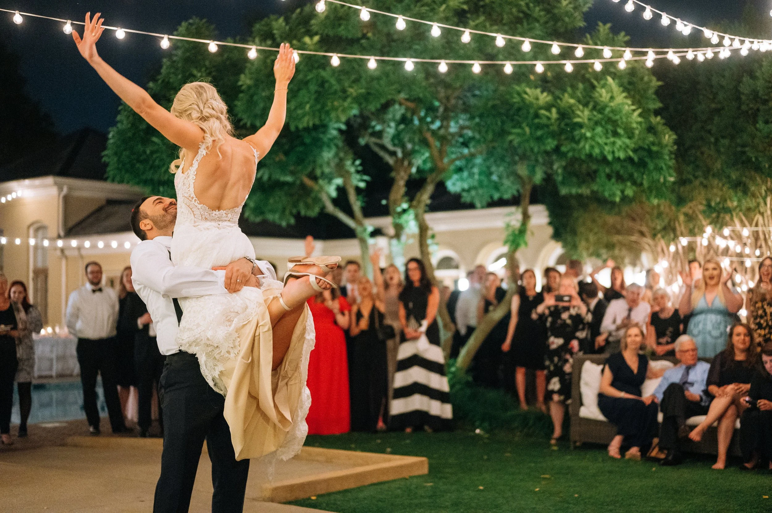A wedding dance celebration outdoors at night with a bride lifted by a groom during their first dance for a Nashville based wedding. Wedding Photography by Sowing Clover Photography.