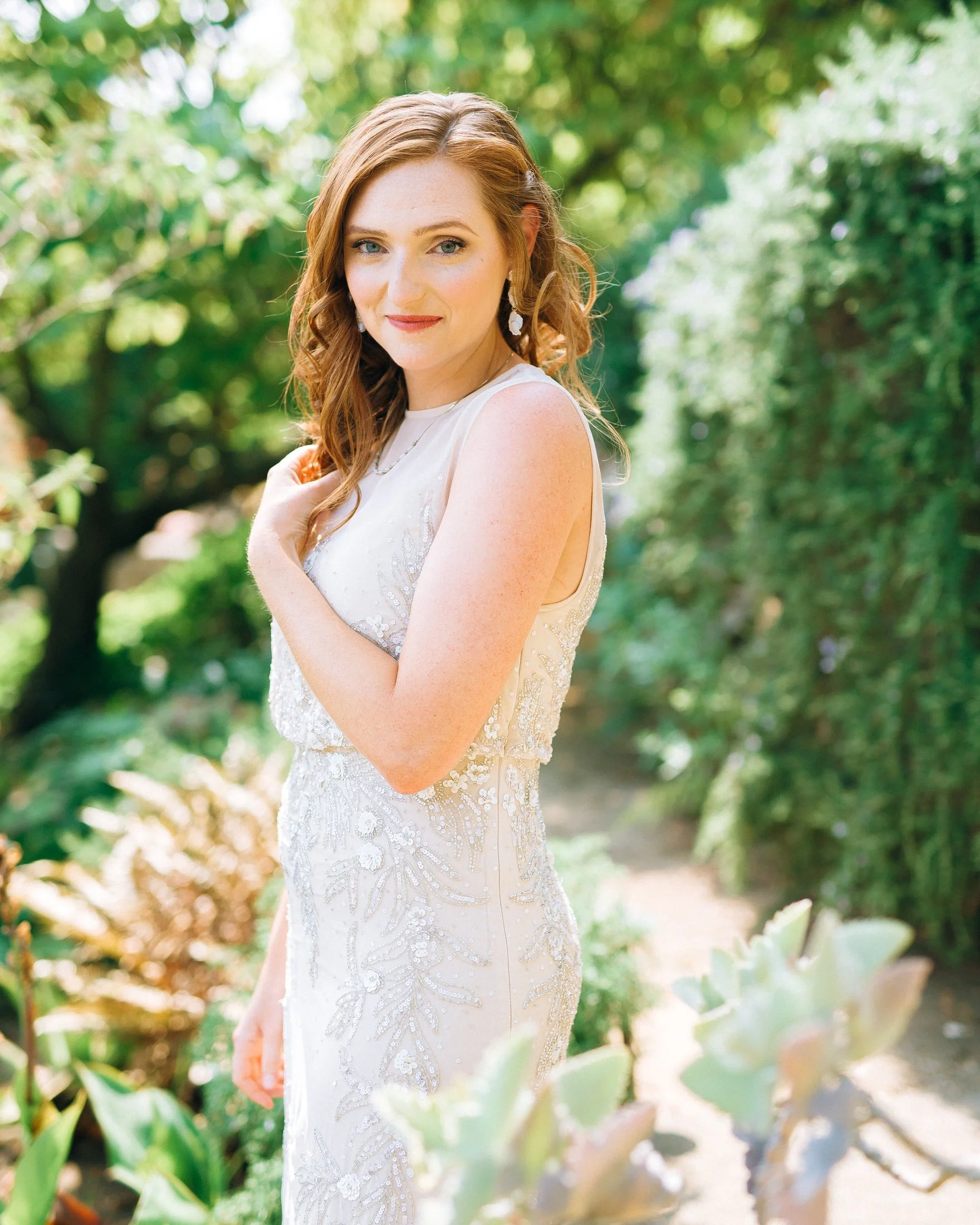 A bride in a white bridal dress standing outdoors among green plants and trees in San Fransisco. Wedding Photography by Sowing Clover Photography.
