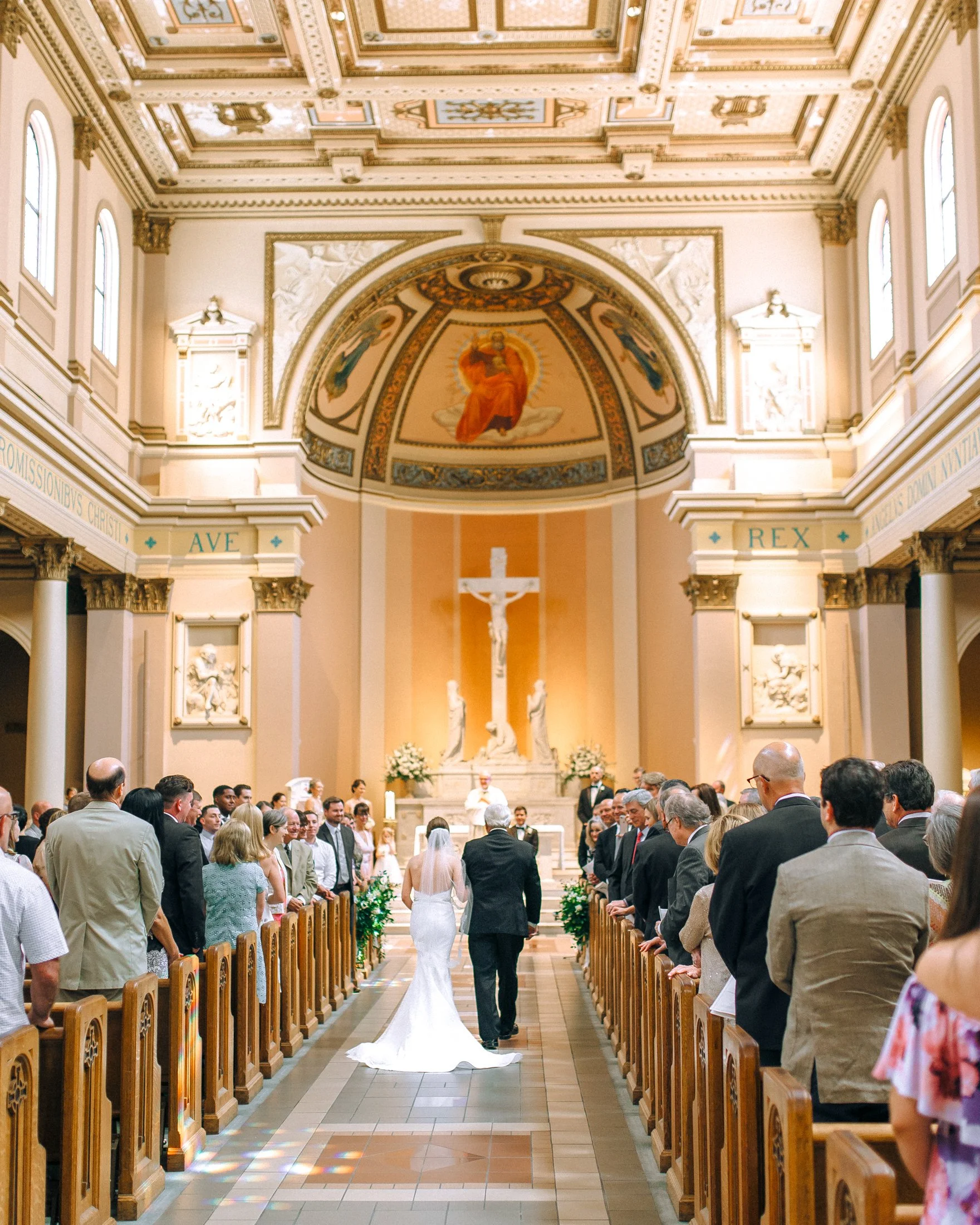 A bride and groom walking down the aisle of a church during their wedding ceremony, with guests standing on both sides watching them at the Cathedral of Incarnation in Nashville. Wedding Photography by Sowing Clover Photography.