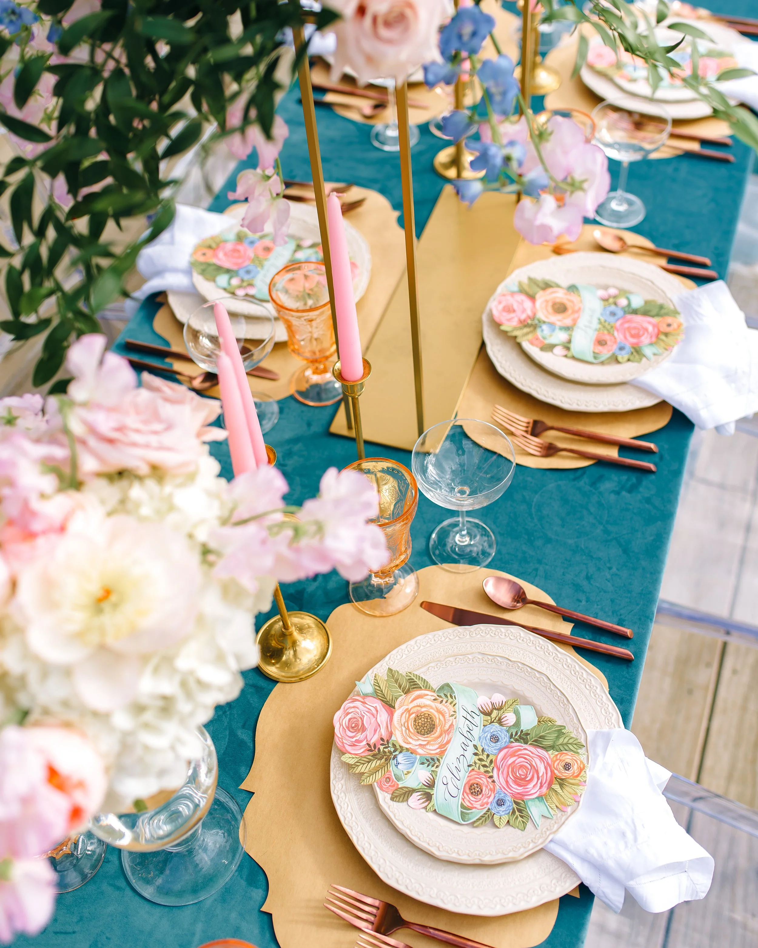 Table setting for a celebration with floral decorations, pink taper candles, floral-themed plates, copper cutlery, and a mirror for reflection outdoors at Glen Ella Springs. Wedding Photography by Sowing Clover Photography.