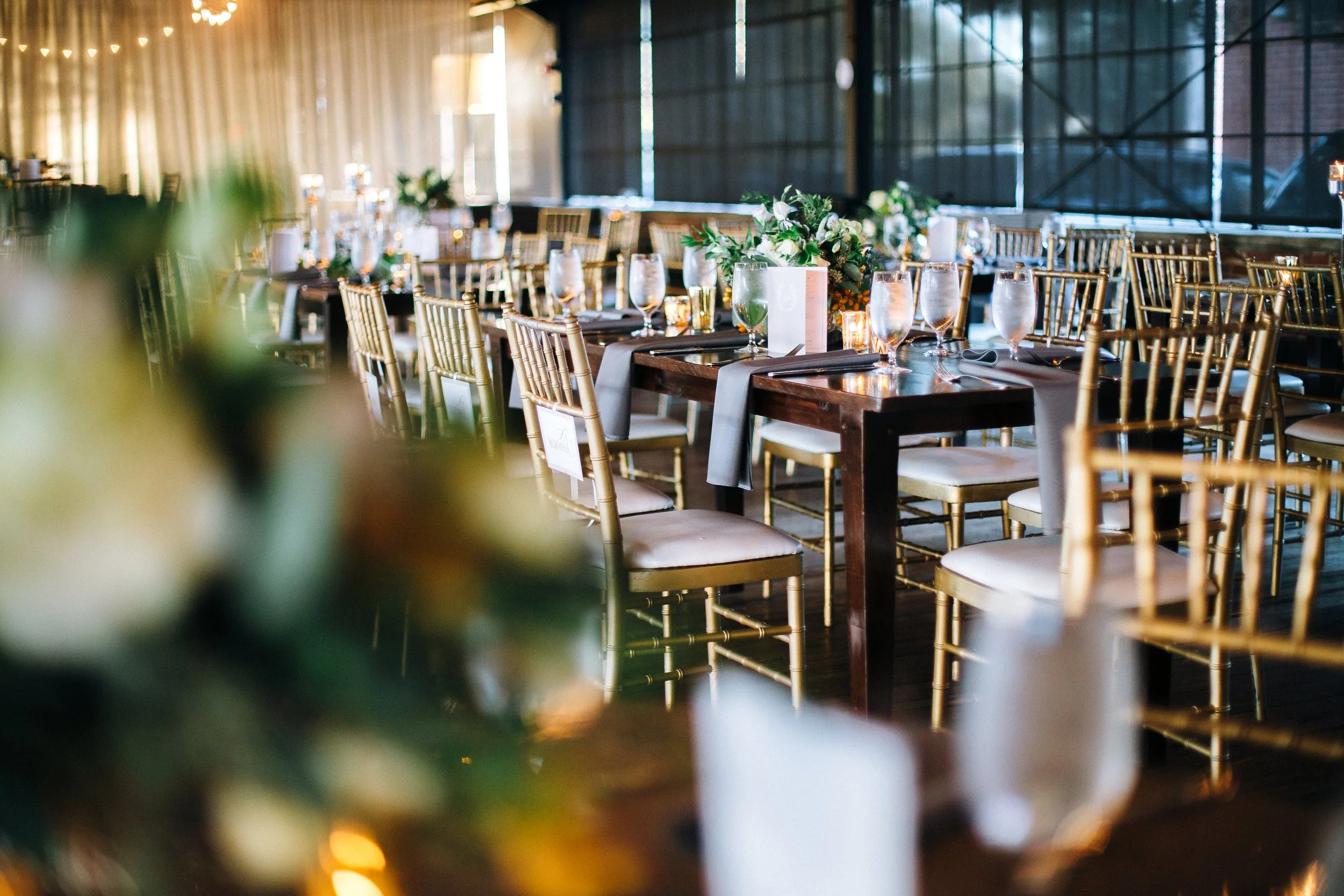 Elegant banquet setup with wooden tables, gold chairs, floral centerpieces, wine glasses, and candles in a decorated event space at Summerhill Studios in Atlanta. Wedding photography by Sowing Clover Photography.