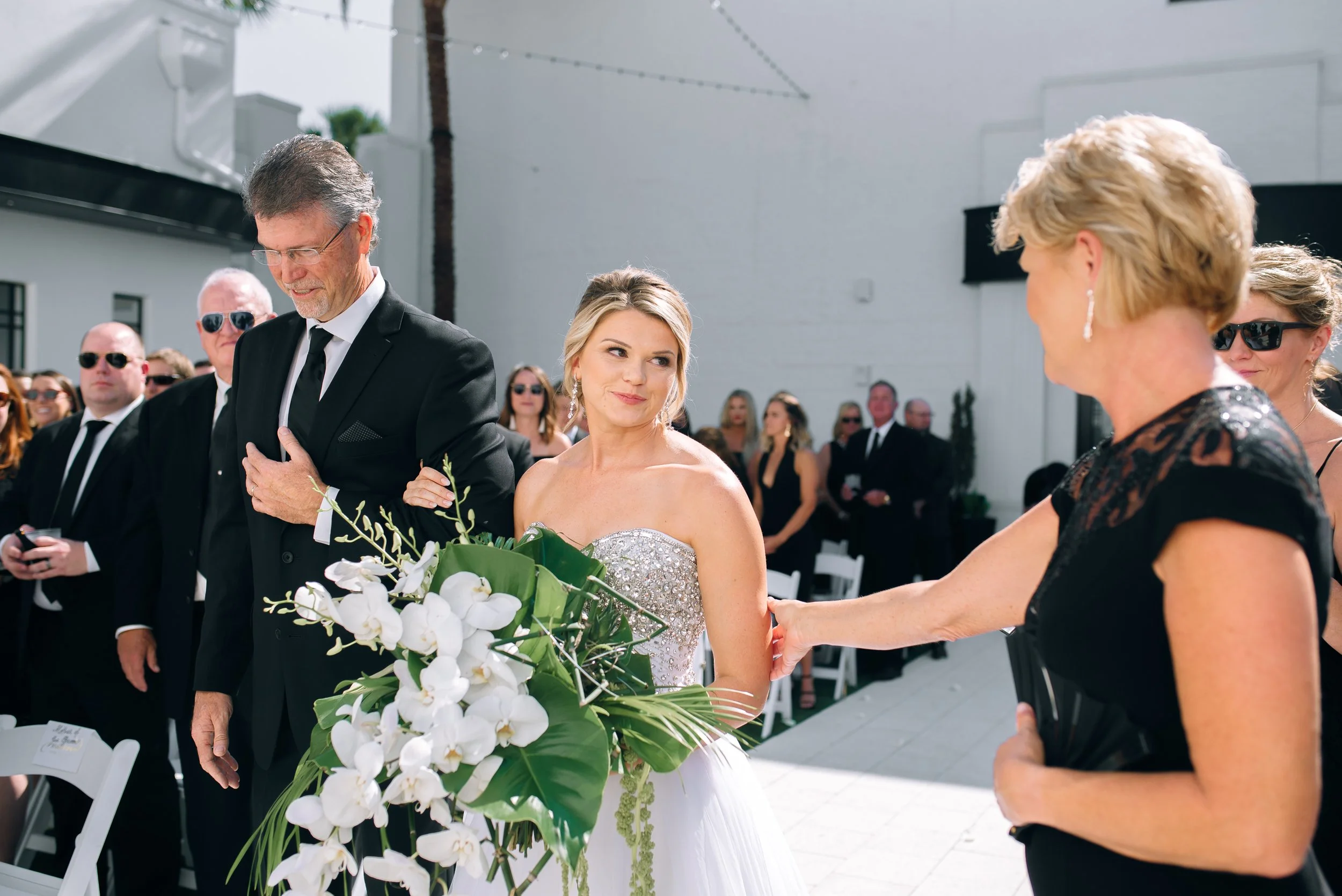 Bride in wedding dress holding a large bouquet of white orchids and greenery during a wedding ceremony at The Clay Theater in Green Cove Springs, Florida. Wedding Photography by Sowing Clover Photography.