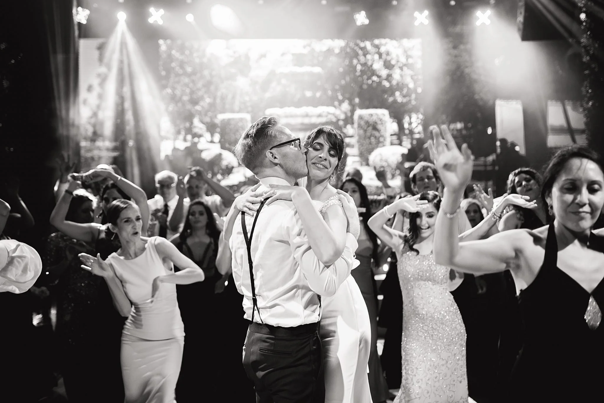 A black and white photo of a couple dancing closely at a celebration, surrounded by people dancing and enjoying the moment in a festive environment for Nashville Wedding Photography