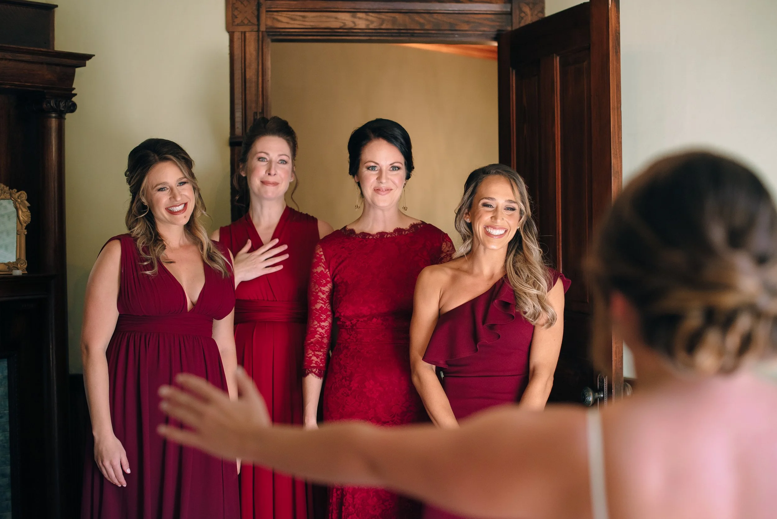 Group of five bridesmaids dressed in red at a wedding reacting to seeing a bride for the bridesmaids reveal at Yaborough Mill wedding Venue. Wedding Photography by Sowing Clover Photography.