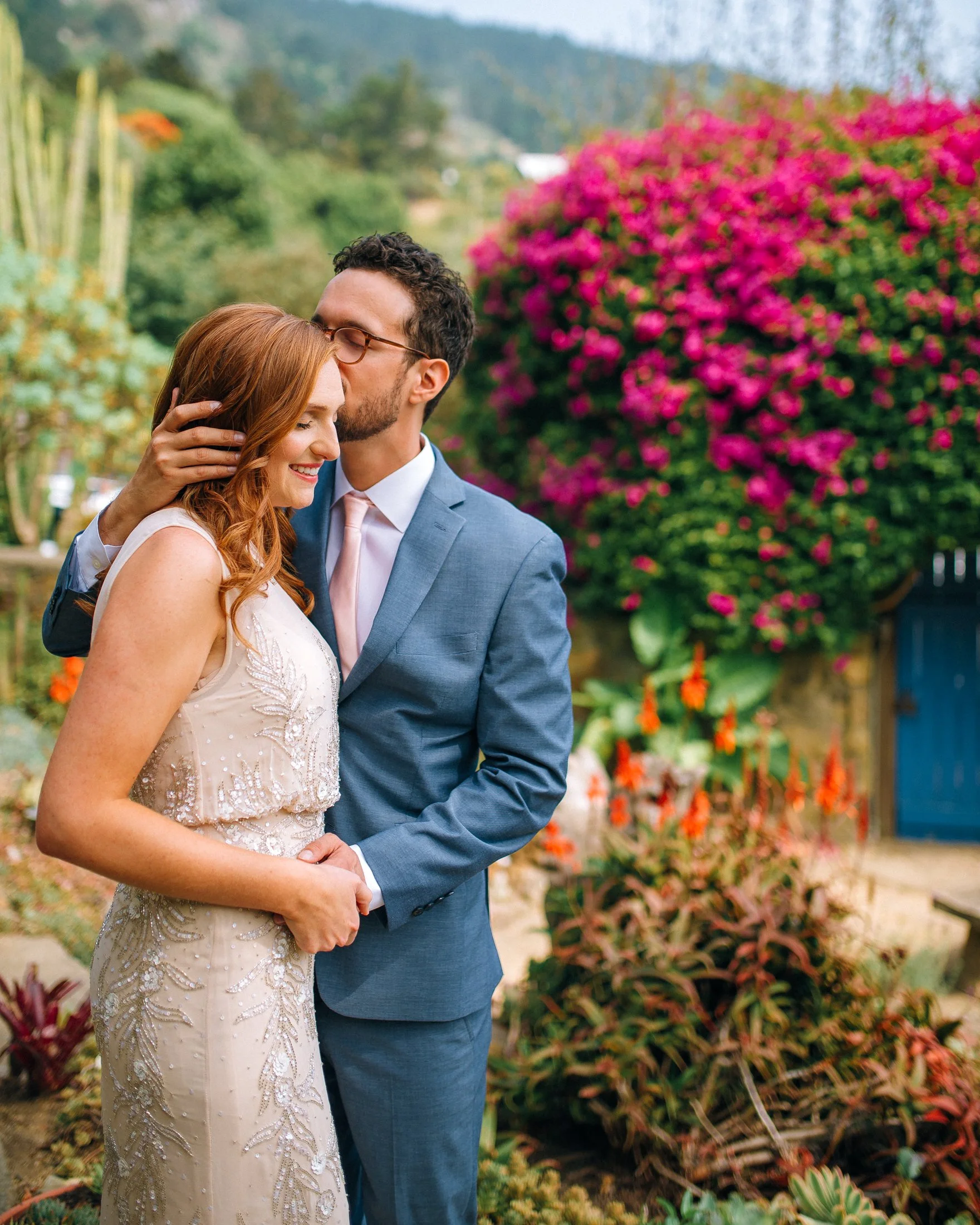 A wedding couple dressed in formal attire sharing a tender moment outdoors near colorful flowering plants and bushes in San Fransisco. Wedding Photography by Sowing Clover Photography.