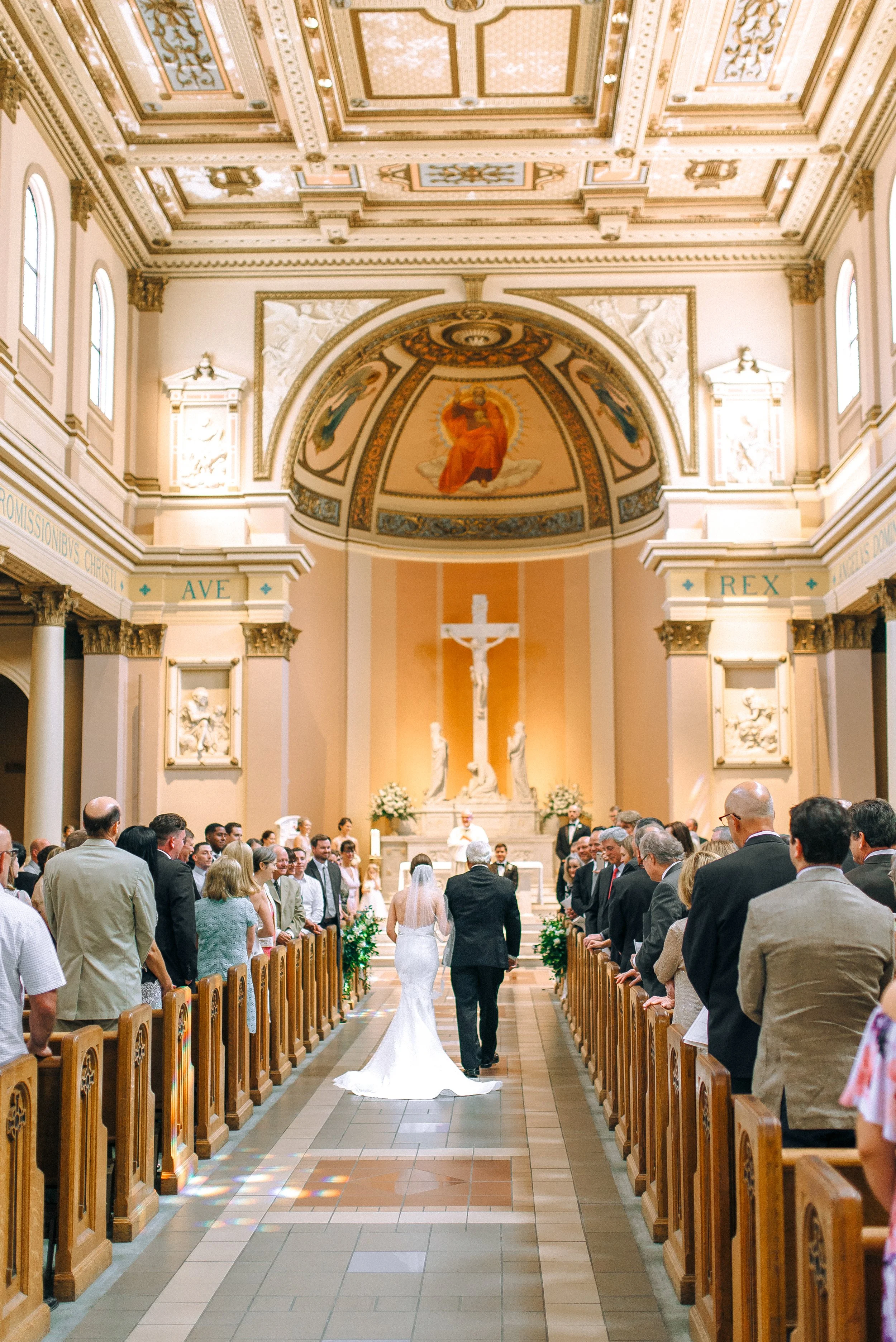 A wedding ceremony inside the cathedral of Incarnation in Nashville with a bride walking down the aisle. Guests are standing on either side of the aisle. Wedding Photography in by Sowing Clover Photography