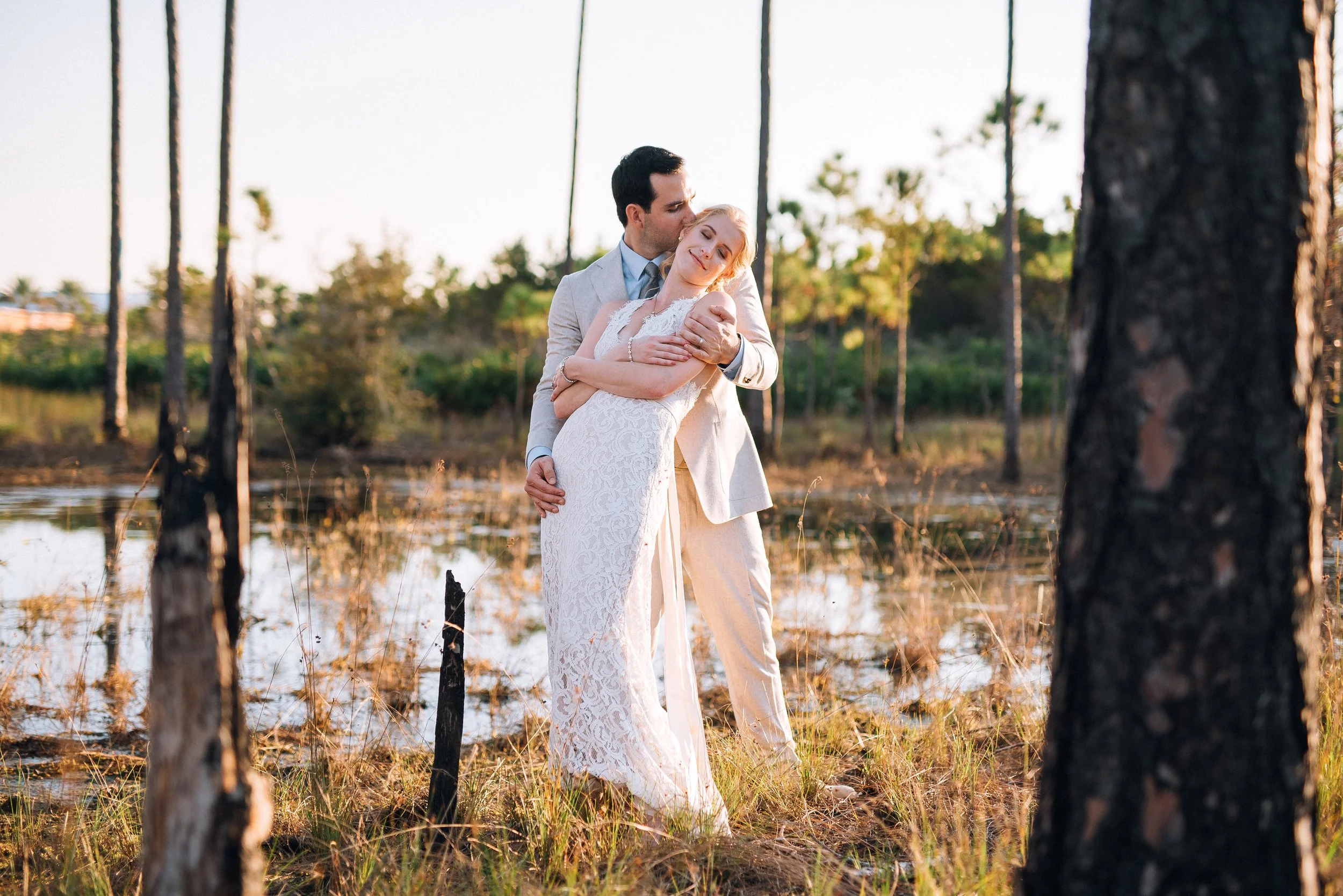 A couple dressed in wedding attire embracing outdoors near water during sunset. Florida wedding Alys Beach. Wedding photography by Sowing Clover Photography.
