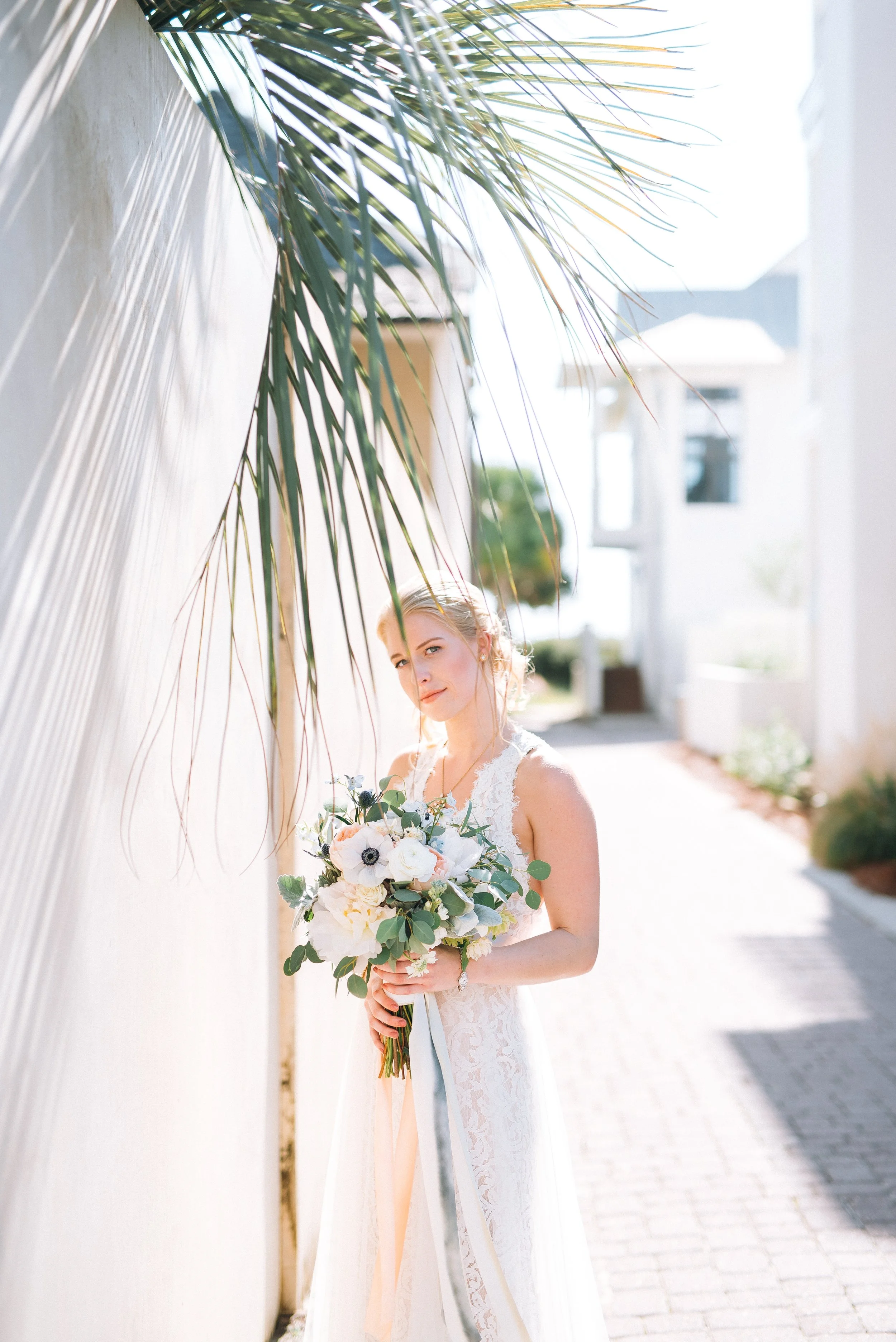 A bride in a white wedding dress holding a bouquet of flowers outside on a sunny day for a beach wedding in Florida. Wedding Photography by Sowing Clover Photography.