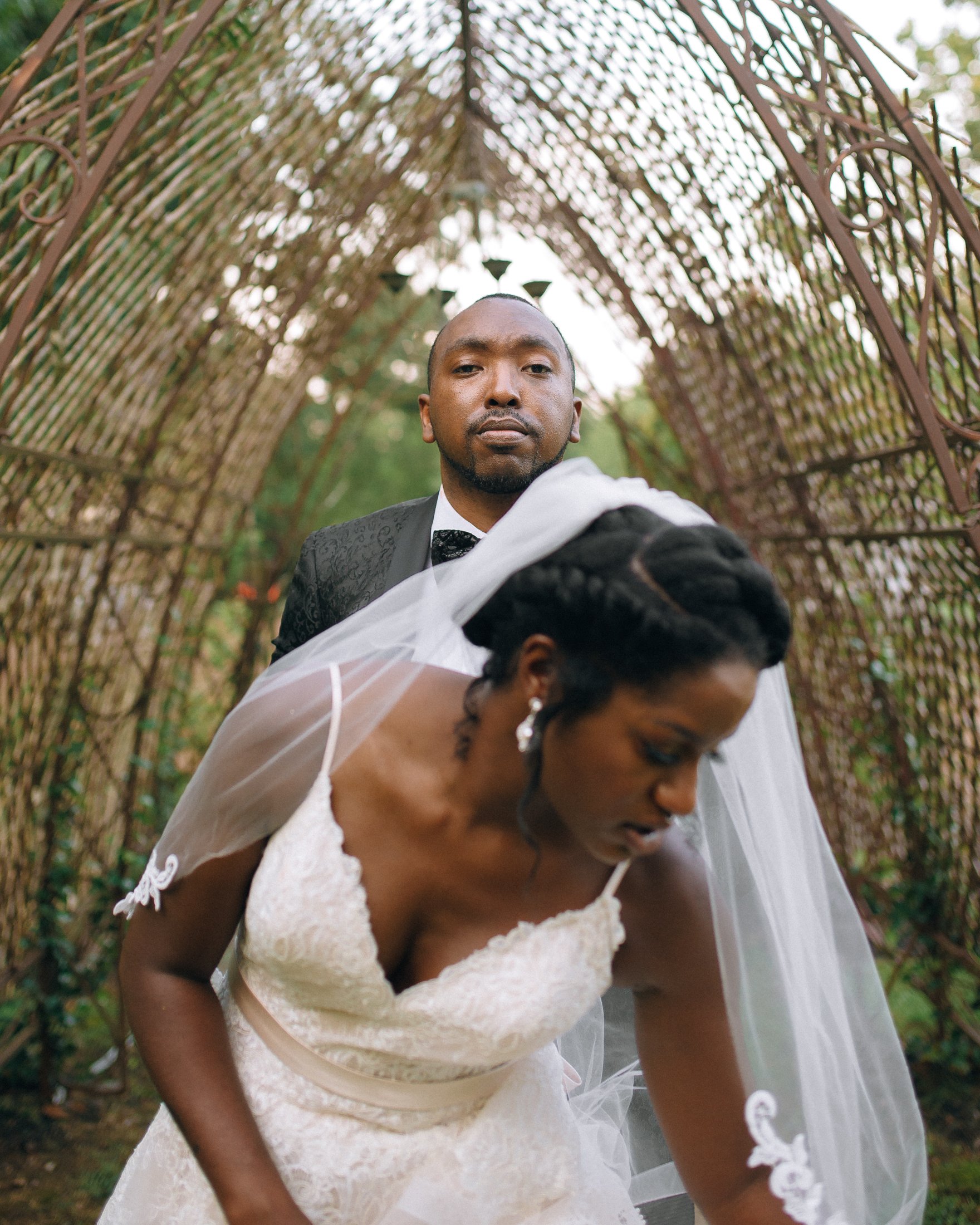 Bride and groom in wedding attire outdoors under a decorative arch of woven branches in Memphis, TN. Wedding Photography by Sowing Clover Photography.