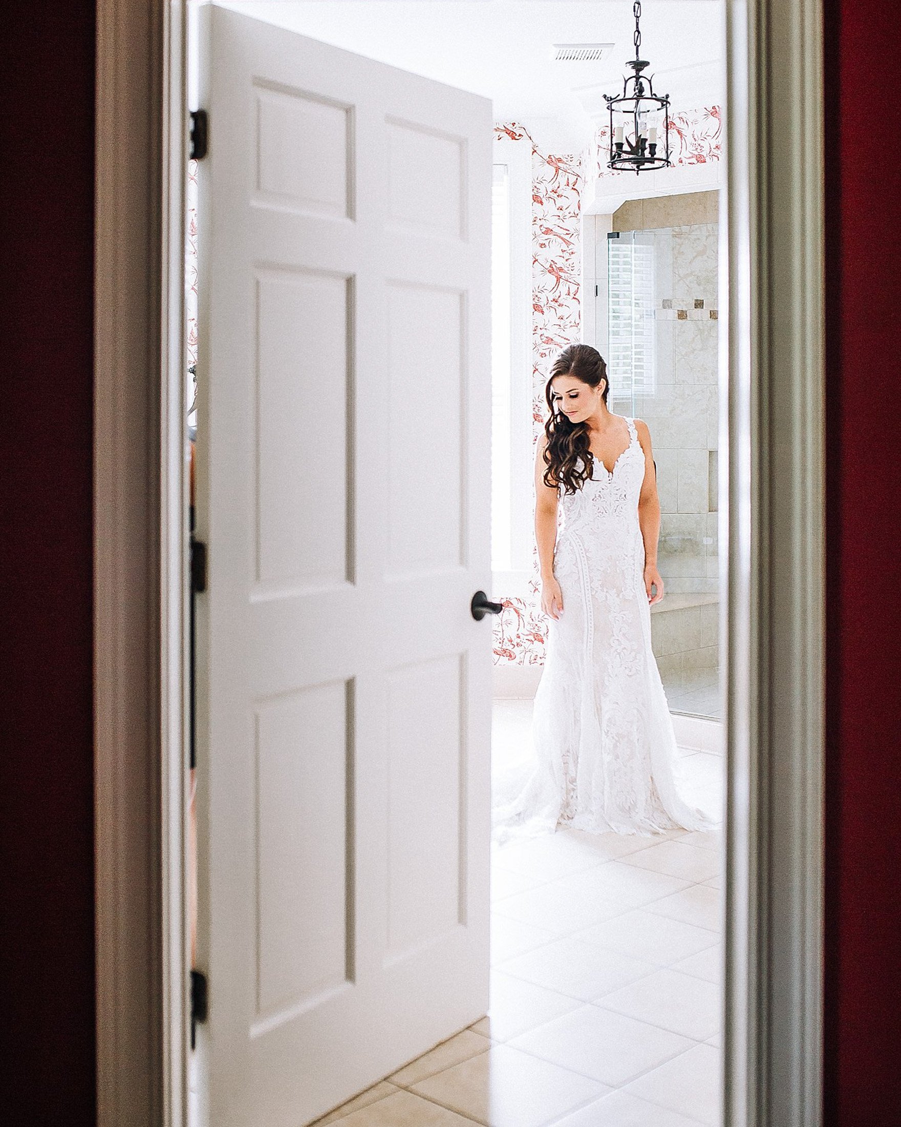 Bride in a white wedding dress looking down in a bathroom, visible through an open door at Barnsley Resort in North Georgia.  Wedding Photography by Sowing Clover Photography.