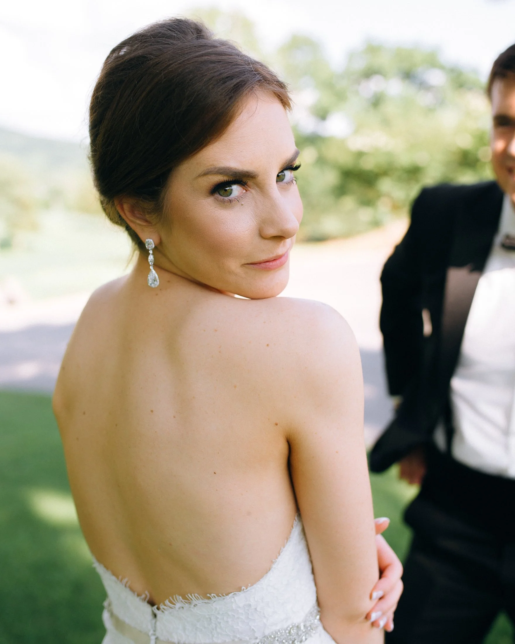 A bride with dark brown hair styled in an elegant updo, wearing diamond earrings, looking over her shoulder at a wedding in Nashville at Brentwood Country Club. Wedding Planner Jayne Bubis.  Wedding Photography by Sowing Clover Photography.