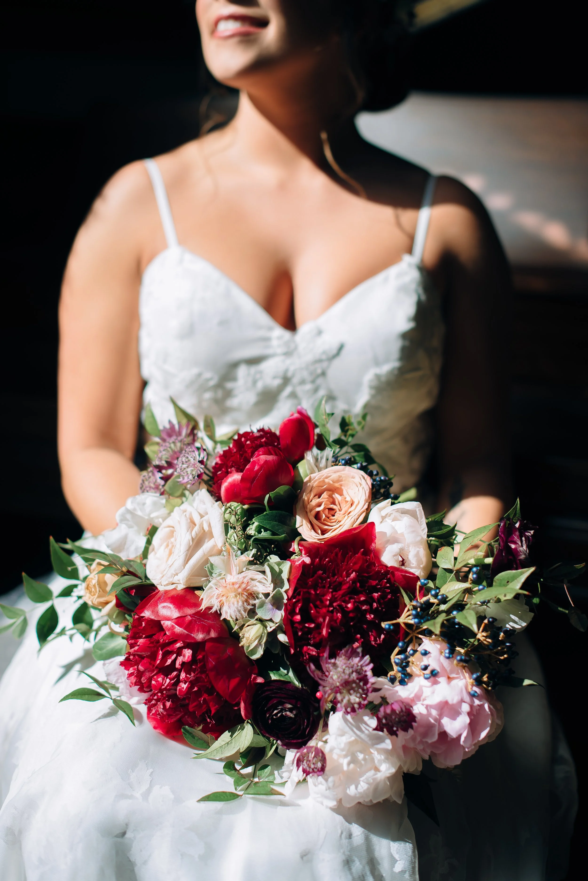 Woman wearing a white dress holding a colorful bouquet of flowers at Yaborough Mill wedding Venue. Wedding Photography by Sowing Clover Photography.