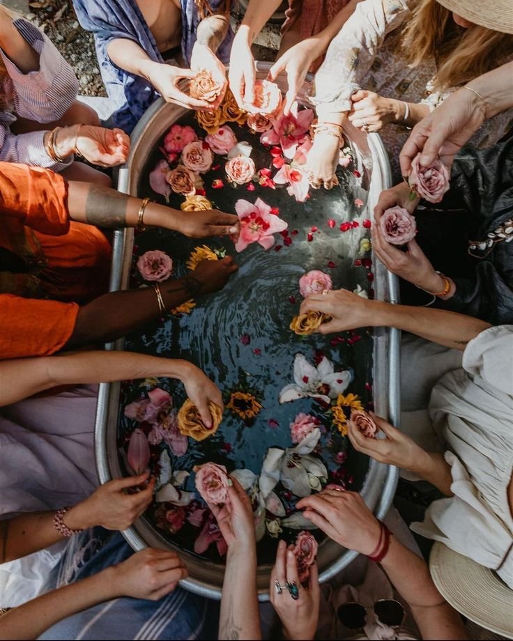 People holding and releasing colorful flowers and petals into a water-filled basin, celebrating a traditional flower ritual representing Ginkgo Wellness Studio community spirit.