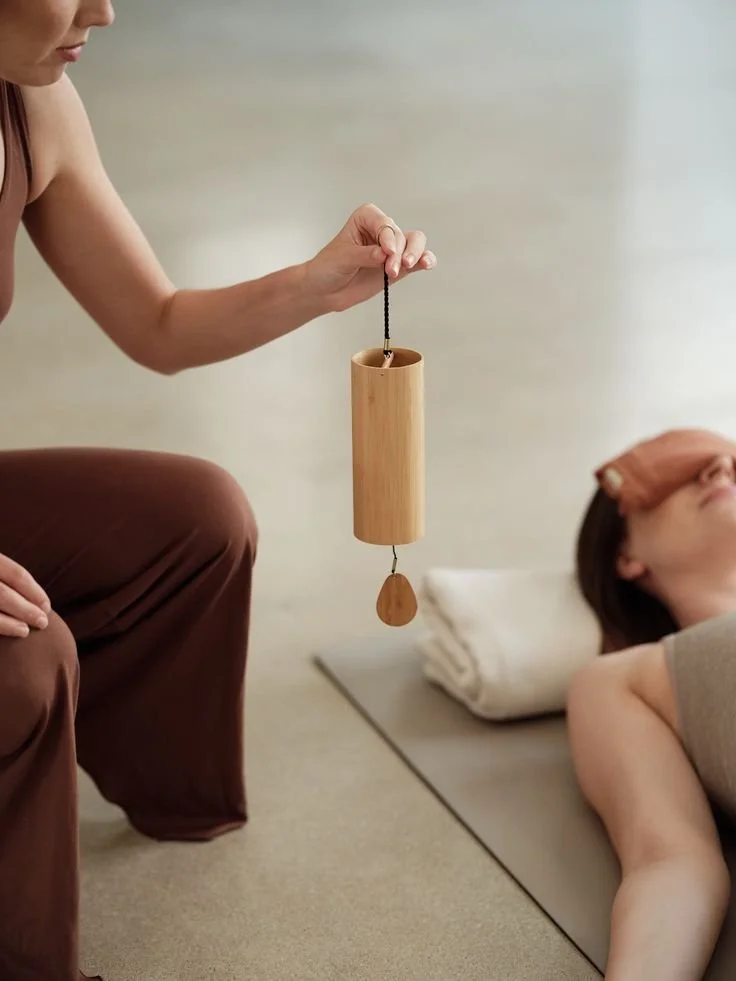 Person holding a chime above a woman lying on a yoga mat in a deep relaxing sound meditation setting.