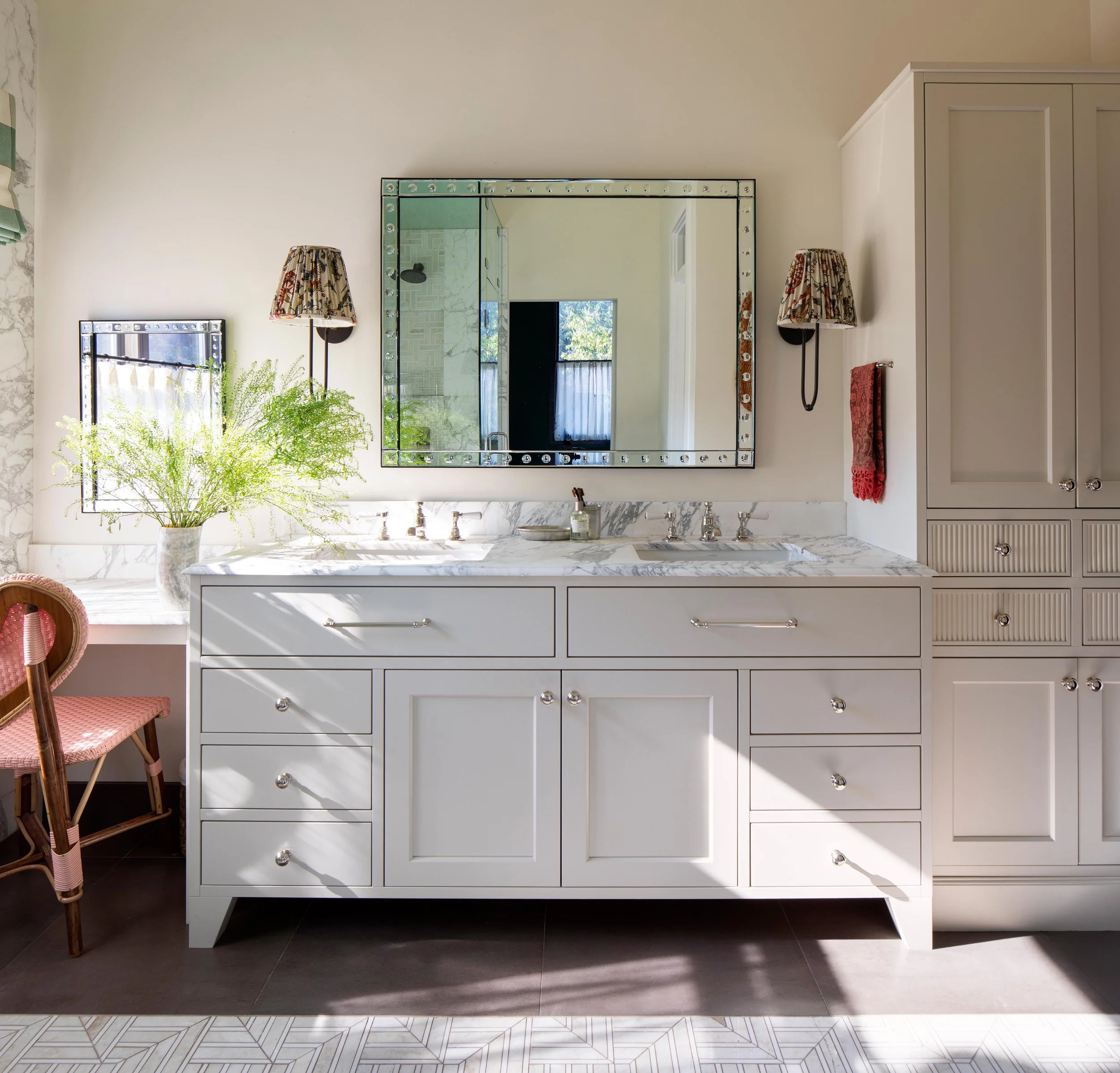 Bright bathroom with white vanity with marble countertop, large mirror, double sinks, wall sconces, green plants, vessel sink, and cabinetry.