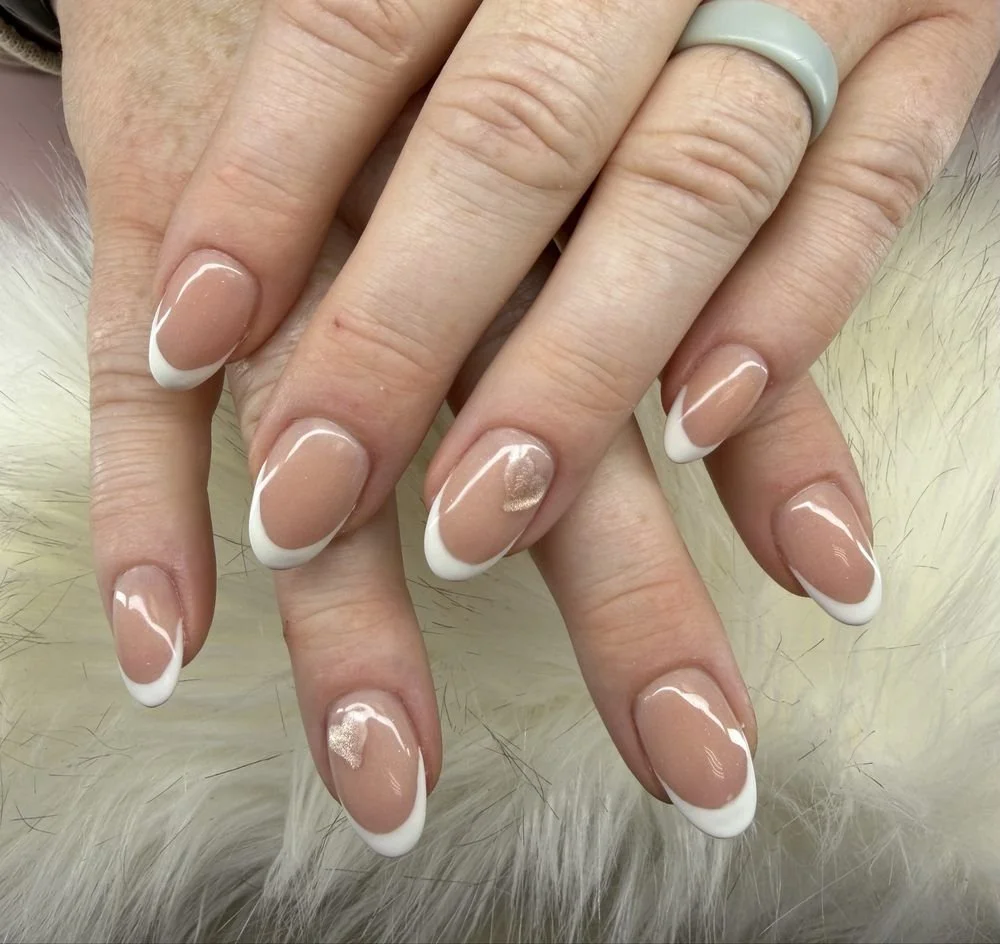 Close-up of hands with freshly manicured nails featuring a French tip design, with a nude base and white tips, on a furry white surface.
