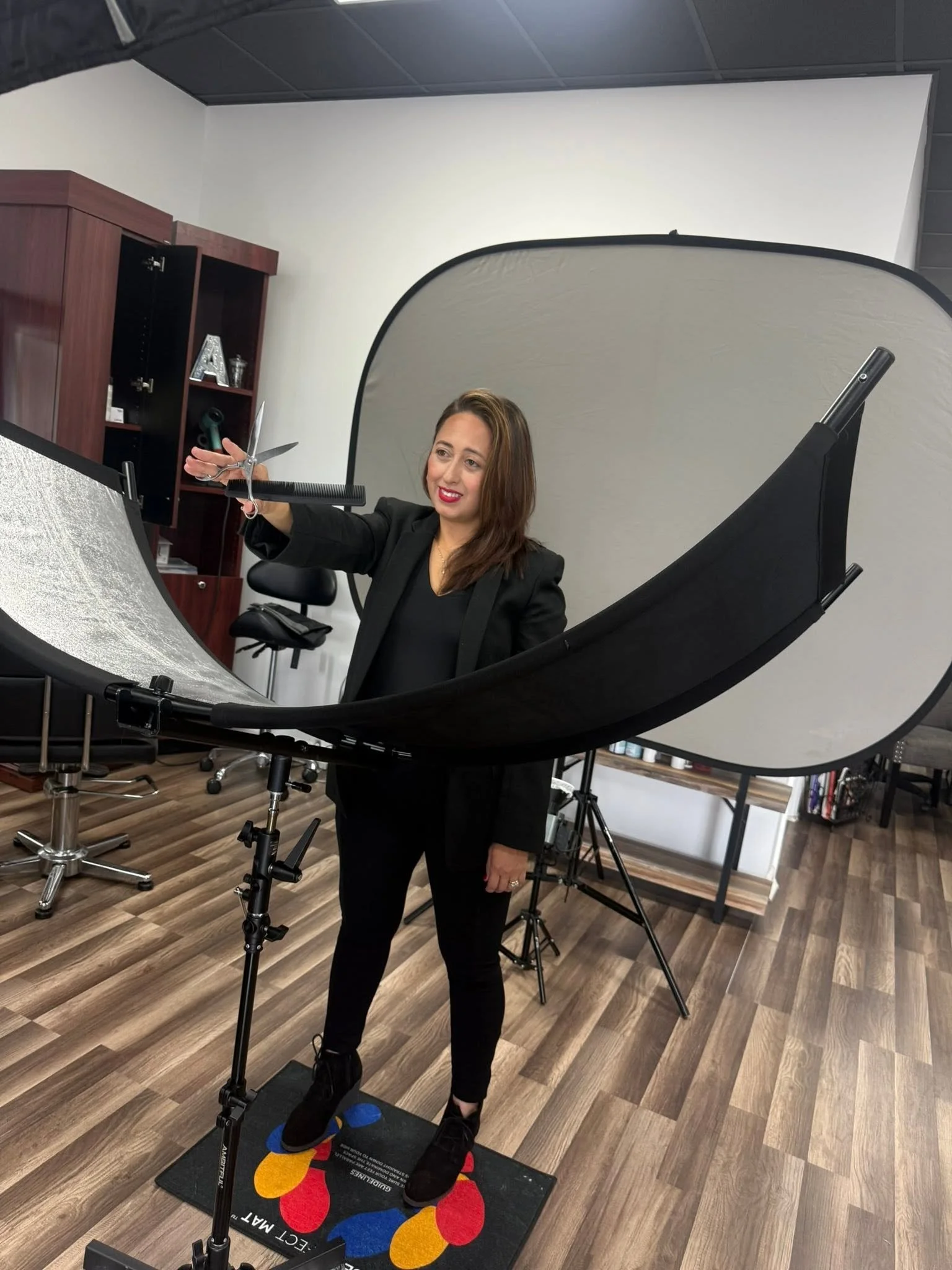 A woman using a light therapy light panel in a professional office setting, standing on a colorful mat with the words "EQUCT MAT" visible, surrounded by office furniture and a white photography backdrop.