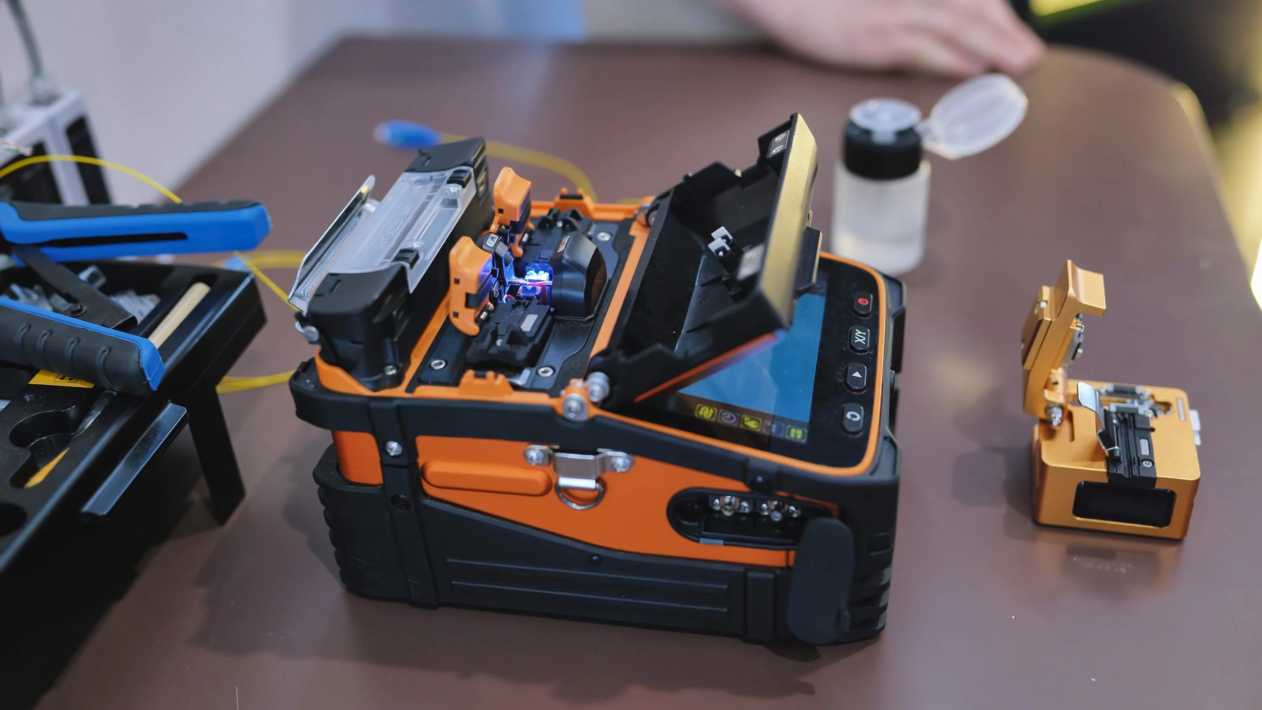 Fiber optic technician using a fusion splicer to join two single-mode fibers, with splice loss measured in fractions of a decibel.