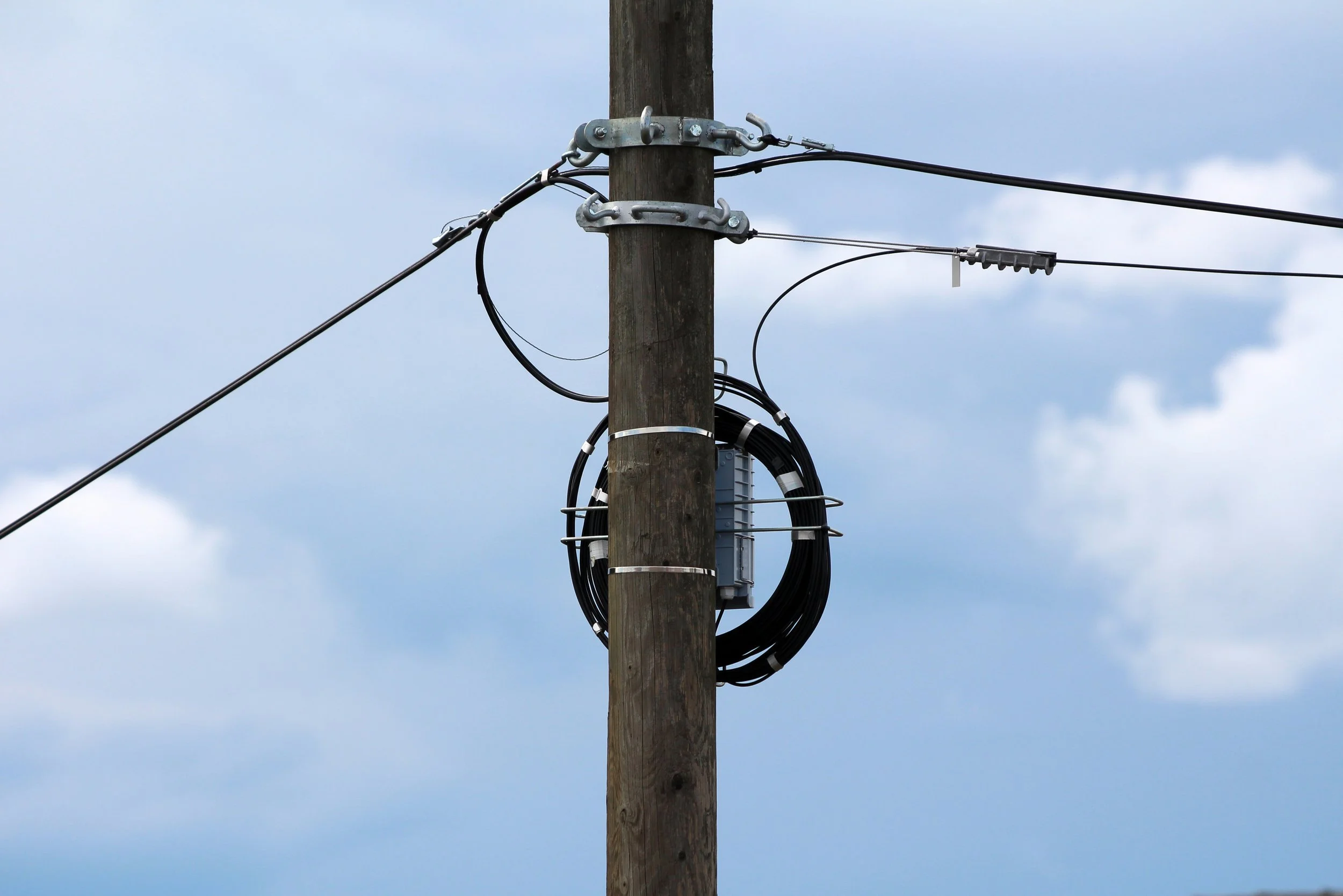 Aerial fiber optic cable installed on a distribution utility pole line against a clear sky.