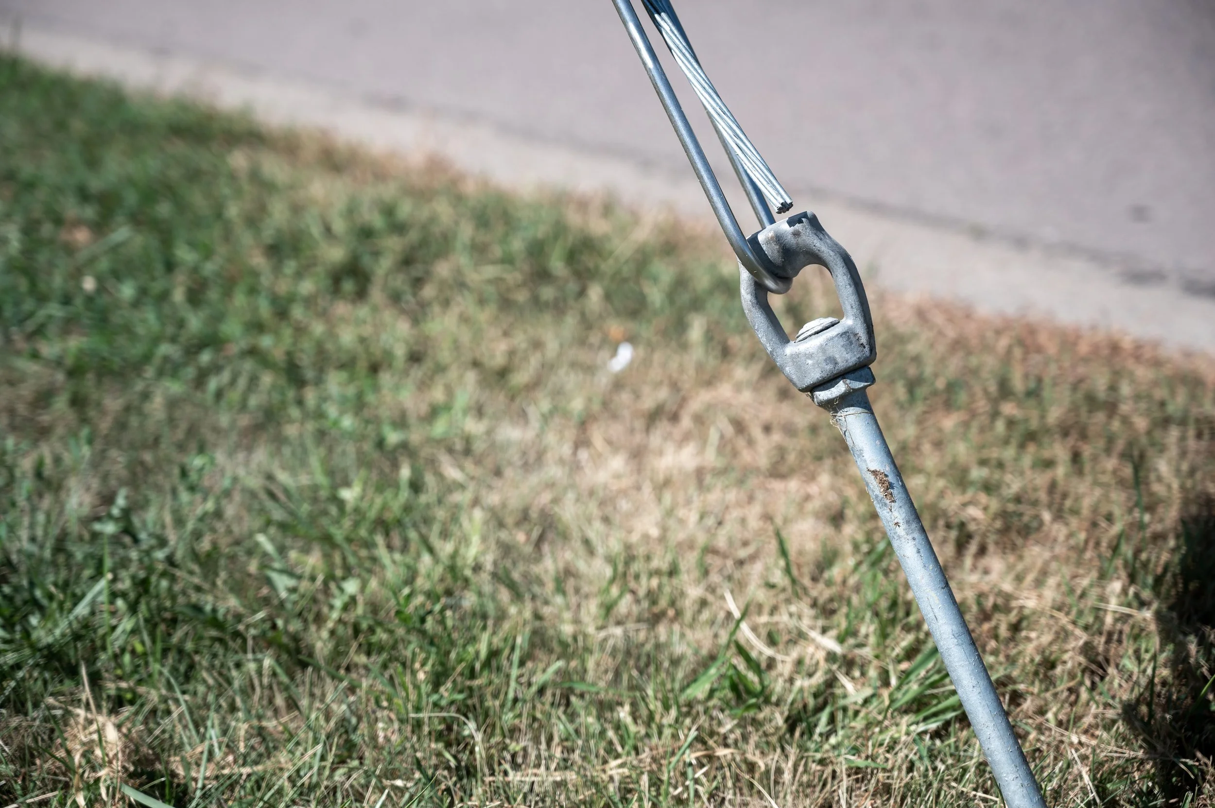A down-guy running from a utility pole to a ground anchor, holding tension on an aerial fiber line at a dead-end