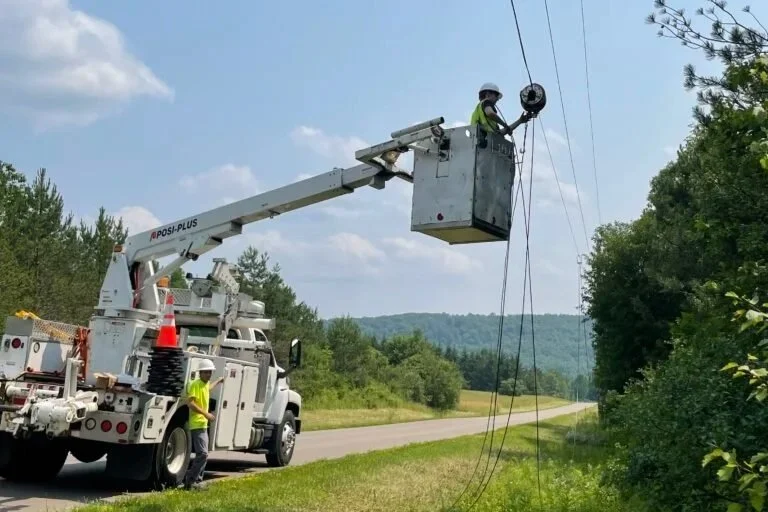 Technician in bucket truck installing aerial fiber optic cable on utility pole