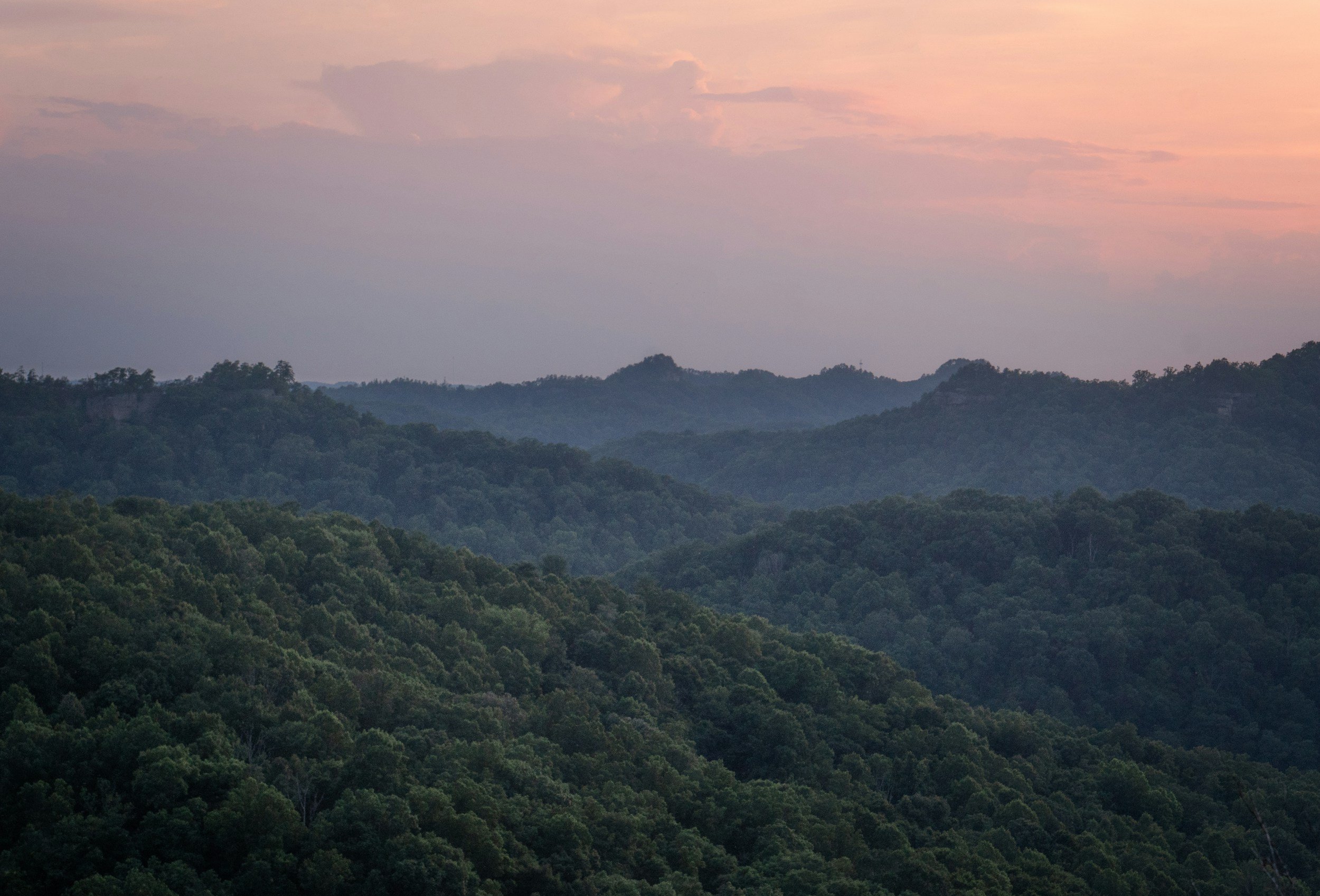 Scenic view of rolling green mountains with pinkish sky and scattered clouds in the background.