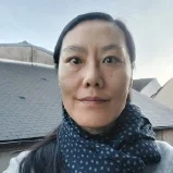 Une femme porte un foulard à pois dans un paysage urbain avec des toits en ardoise et un ciel clair.