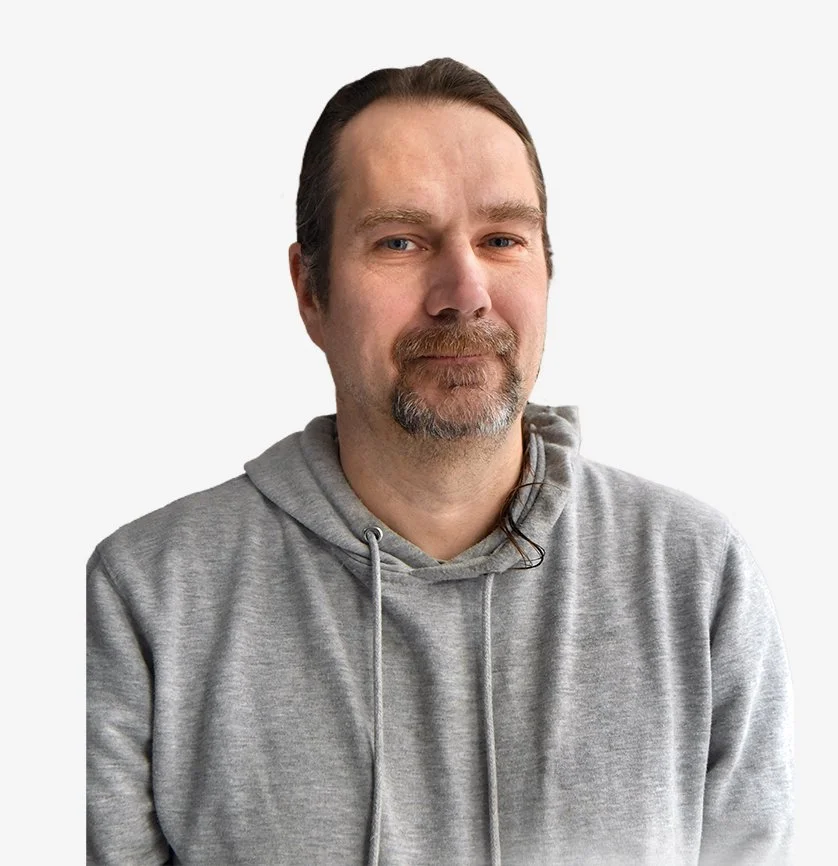 Photographie d'un homme de face, léger sourire bouche fermée. Il a les cheveux longs attachés en arrière, châtains/bruns. Bouc grisonnant. Il est habillé d'un sweat shirt gris.