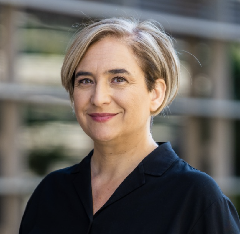 Une femme avec des cheveux bouclés bruns et portant une veste beige devant un fond violet avec du texte blanc.