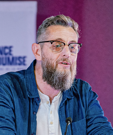 Homme portant des lunettes de vue, une veste bleue et un haut blanc.