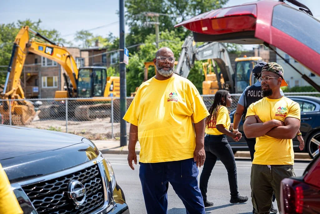 People wearing yellow shirts participating in a community event near a construction site, with excavators in the background.