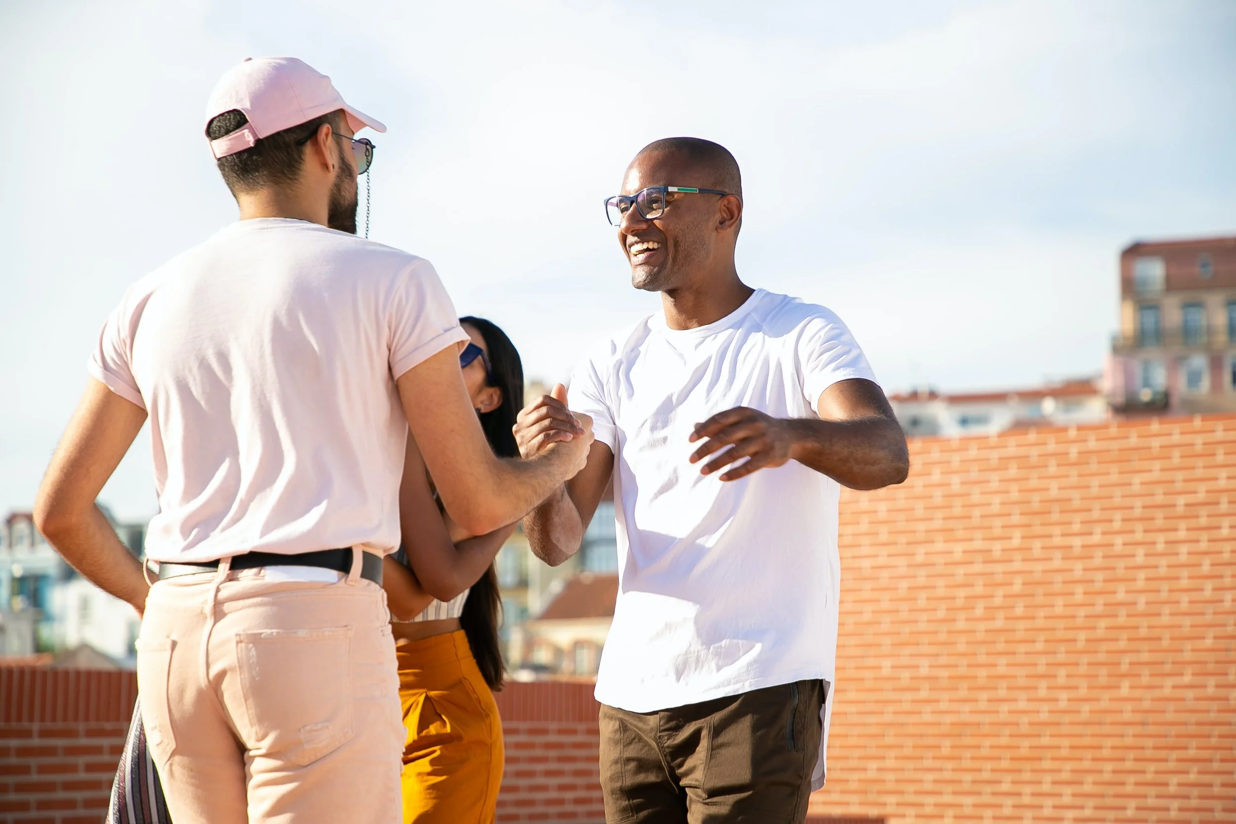 Four friends happily socializing outdoors on a sunny day, with a brick wall and city buildings in the background.