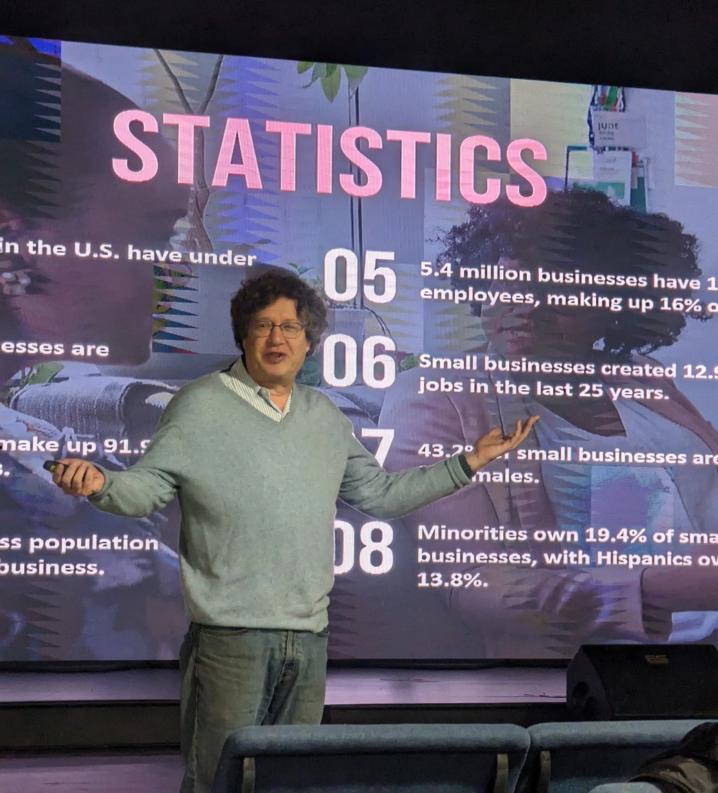 A man standing in front of a presentation slide with statistics about small businesses in the U.S., holding a remote control, gesturing with one hand.