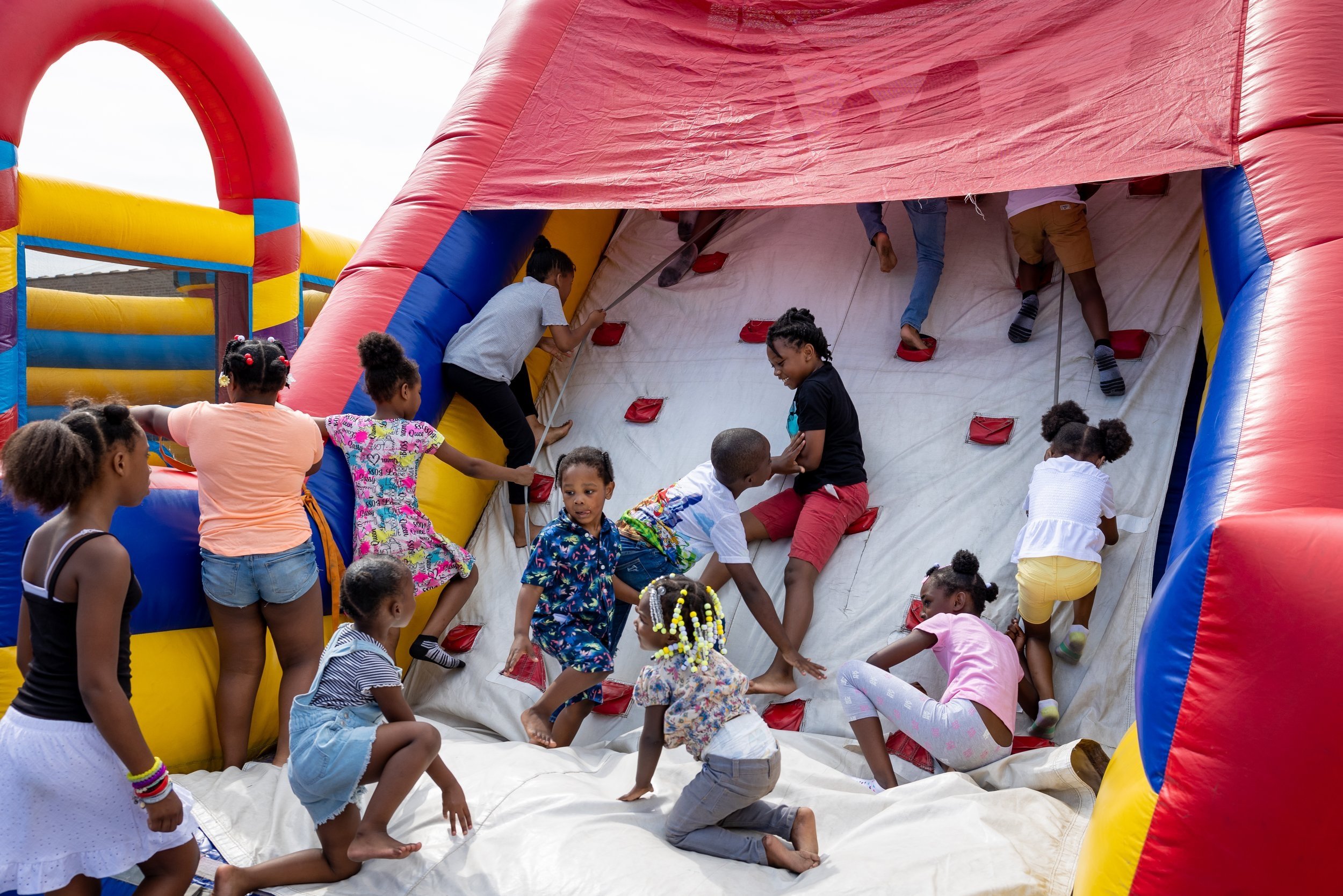 Children playing on an inflatable bounce house with a climbing wall at an outdoor event.