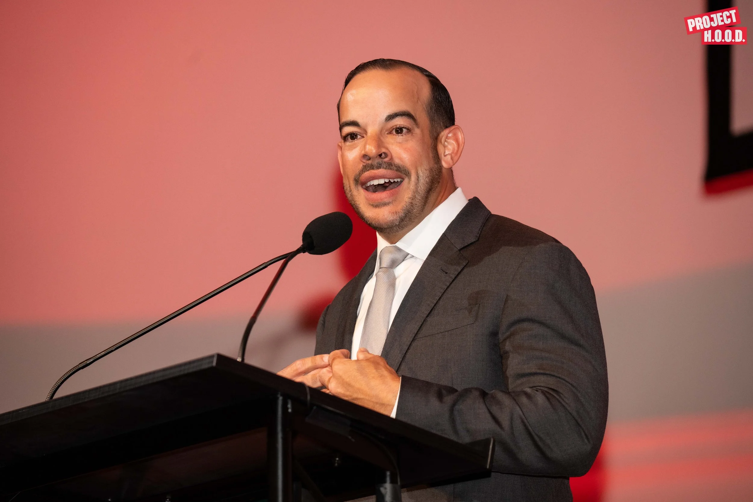 A man in a gray suit and light-colored tie speaking at a microphone.