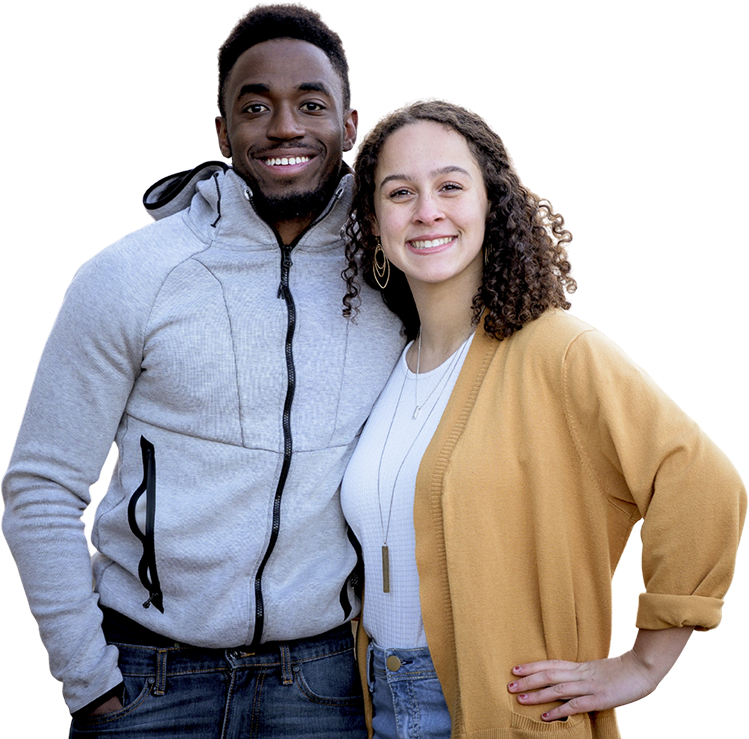 A smiling young man and woman standing close together, smiling at the camera. The man wears a light gray zip-up hoodie and jeans, and the woman wears a mustard yellow cardigan over a white top with jeans.