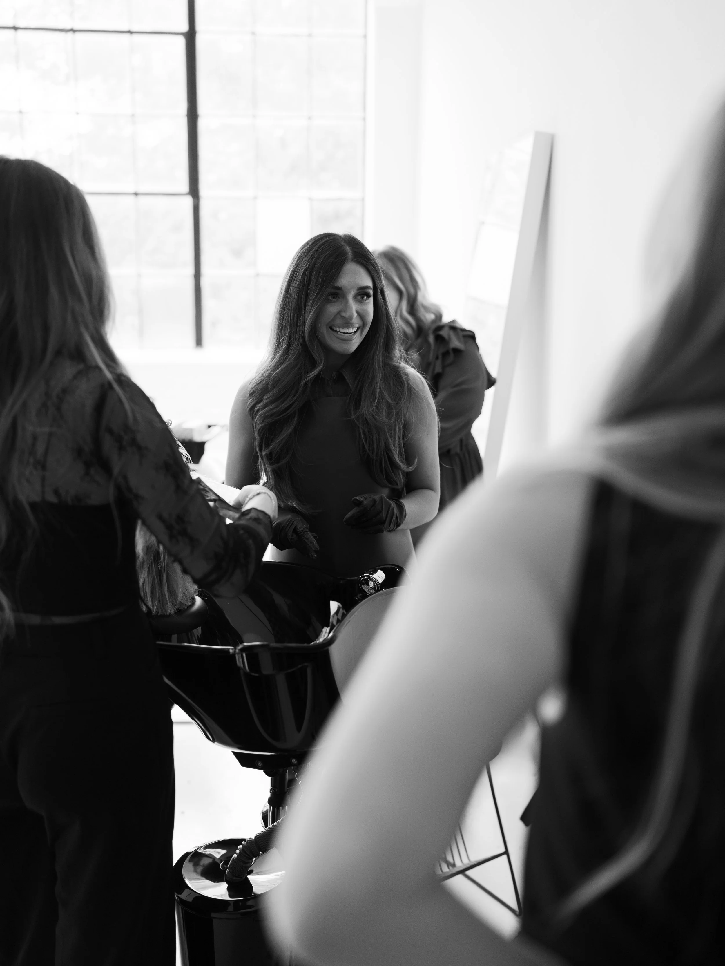 Group of women engaging in a conversation in a bright room with large windows, some wearing black gloves, some smiling.