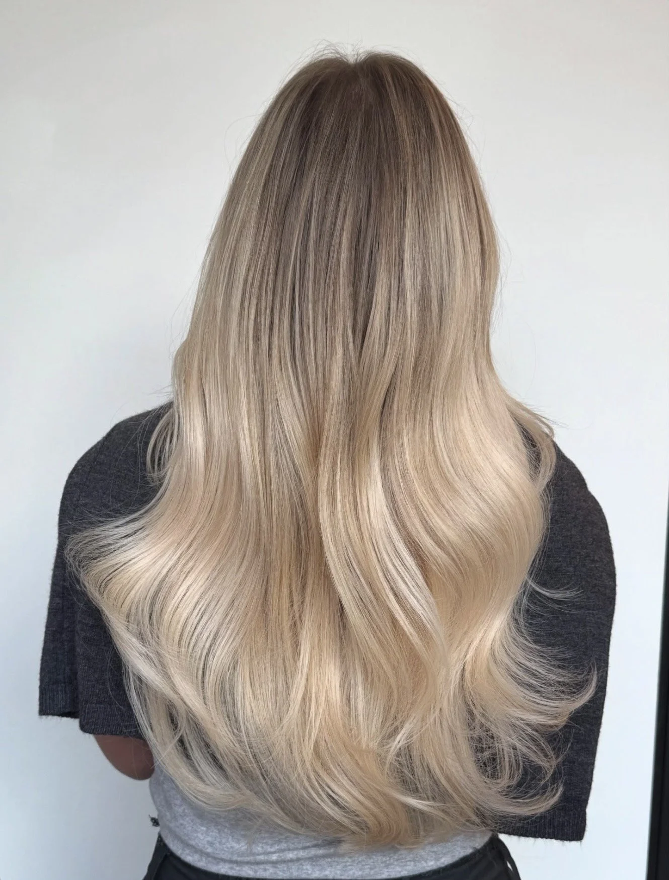 Back of a person with long, wavy blonde hair that transitions from ash brown at the roots to platinum blonde at the ends.