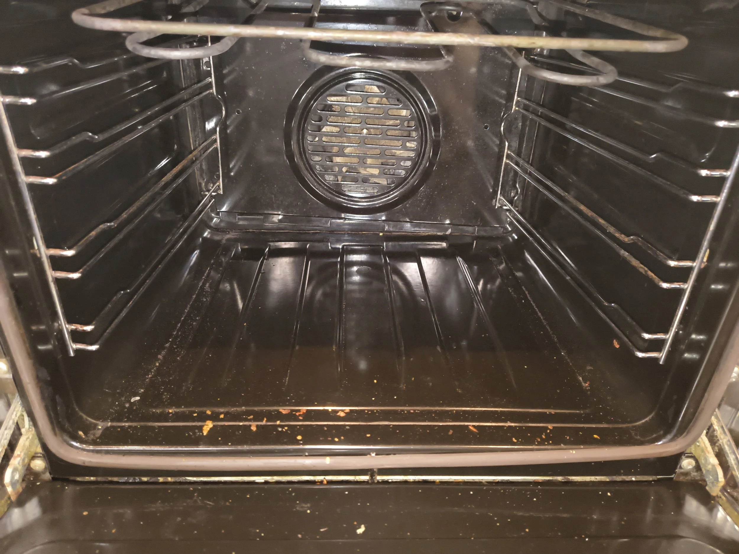 Empty black oven with some food crumbs and stains at the bottom.